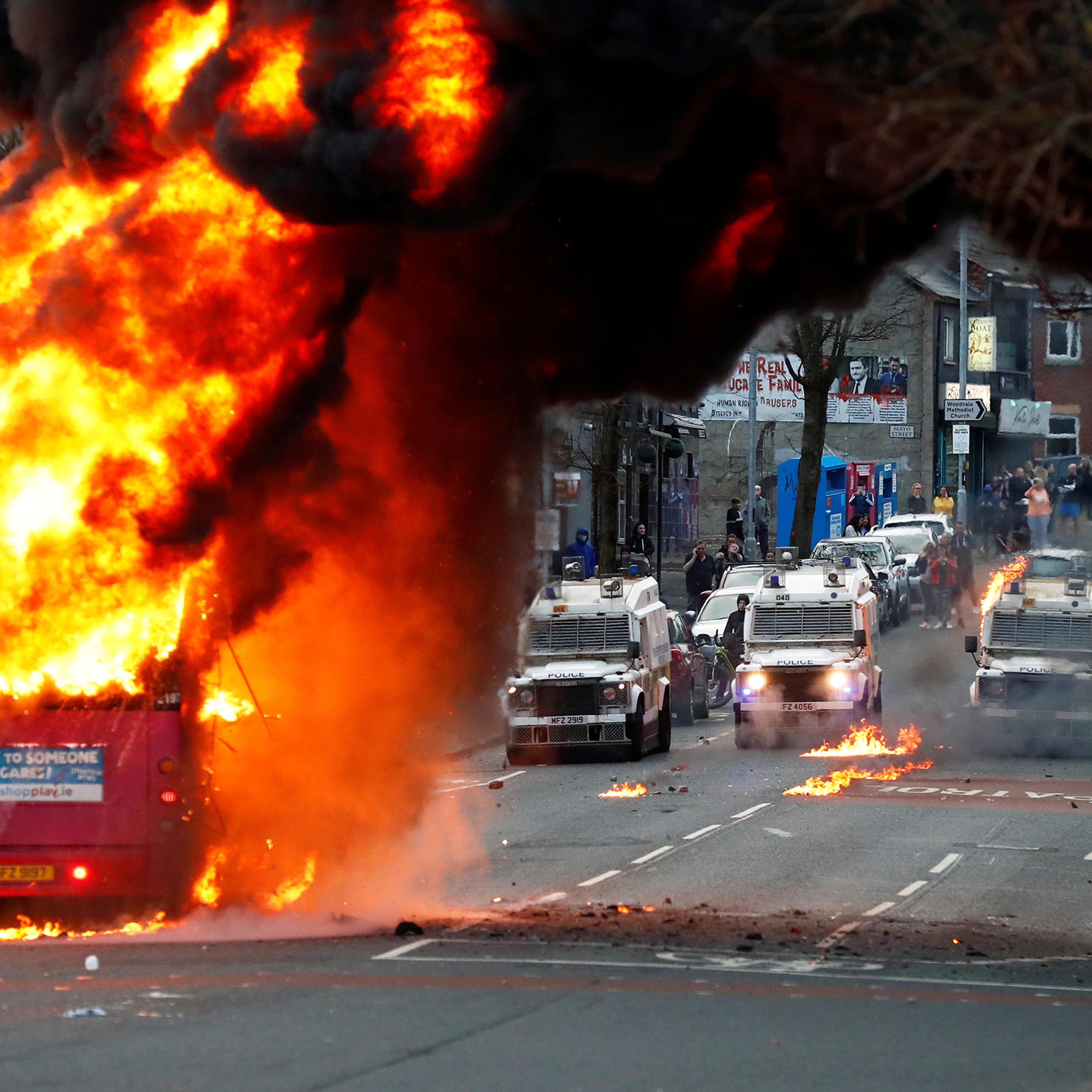 Police vehicles are seen behind a hijacked bus burns on the Shankill Road as protests continue in Belfast, Northern Ireland, April 7.