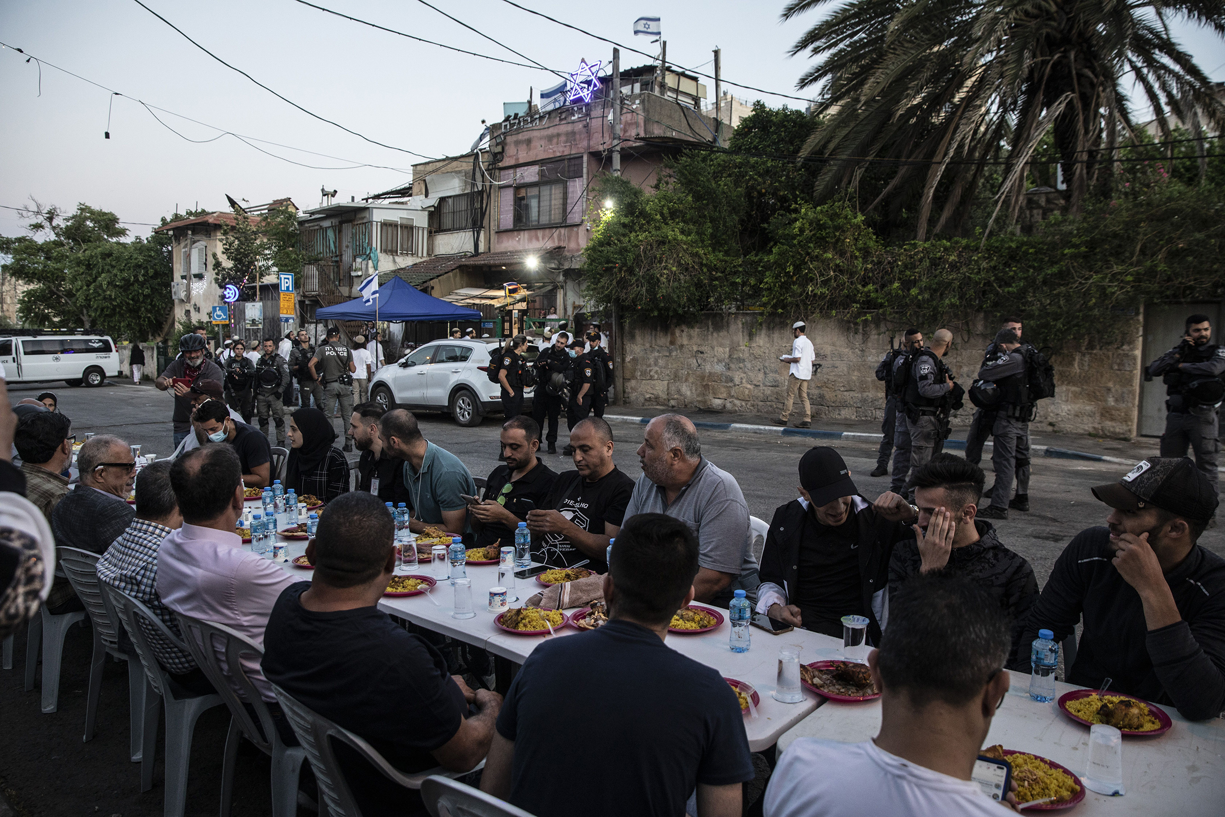 Palestinians sit at a large table to break the fast during Ramadan as Israeli border police guard Jewish settlers, outside one of the homes they have taken over from a Palestinian family and by other homes of Palestinians facing eviction, in the East Jer
