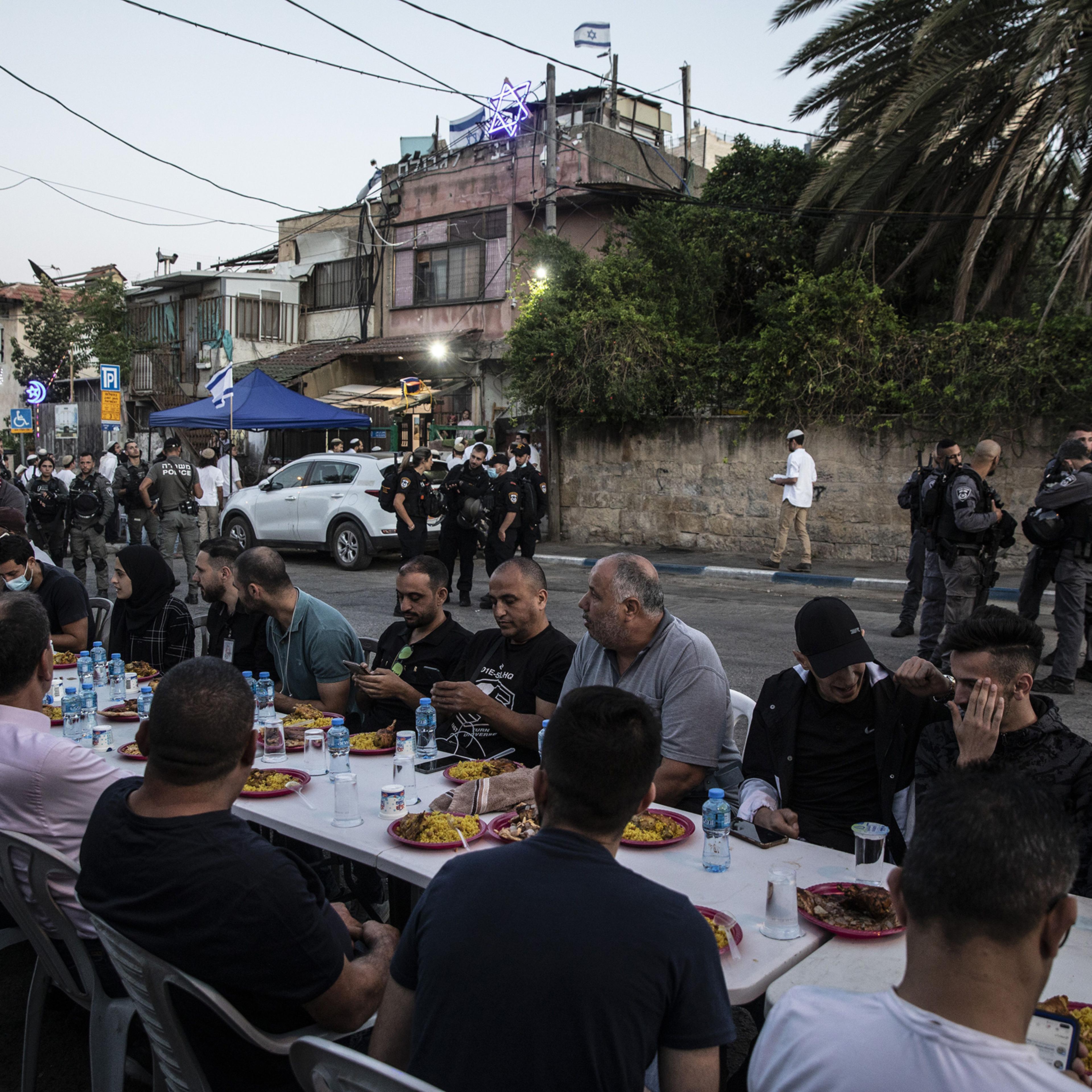 Palestinians sit at a large table to break the fast during Ramadan as Israeli border police guard Jewish settlers, outside one of the homes they have taken over from a Palestinian family and by other homes of Palestinians facing eviction, in the East Jer