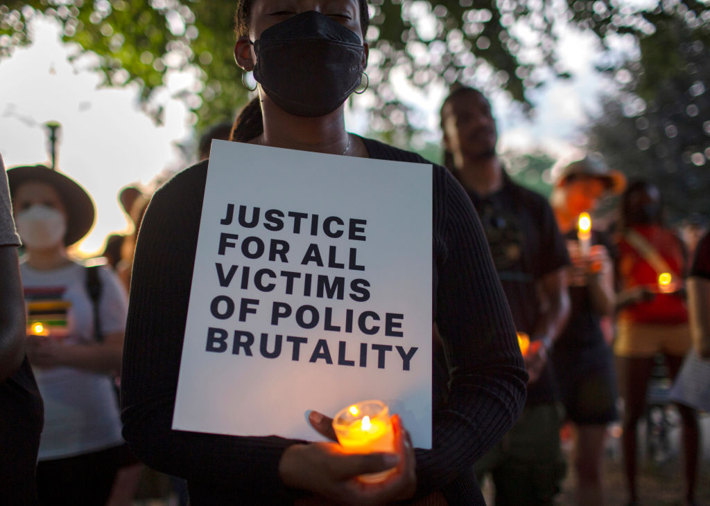 A demonstrator holding a candle and a sign with Justice For