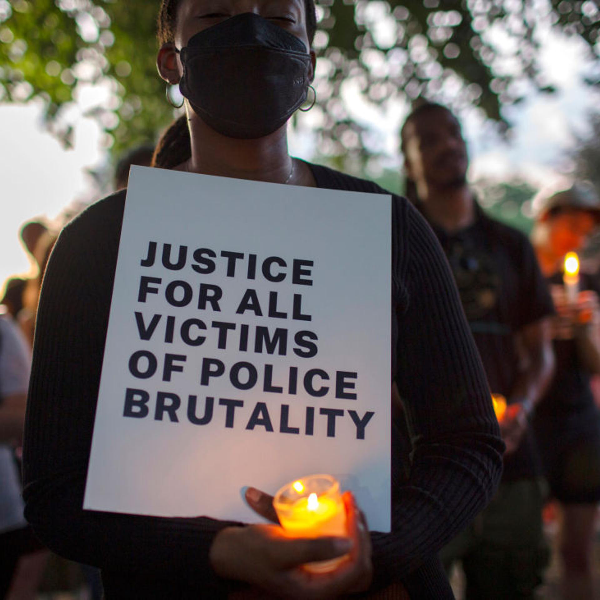 A demonstrator holding a candle and a sign with Justice For