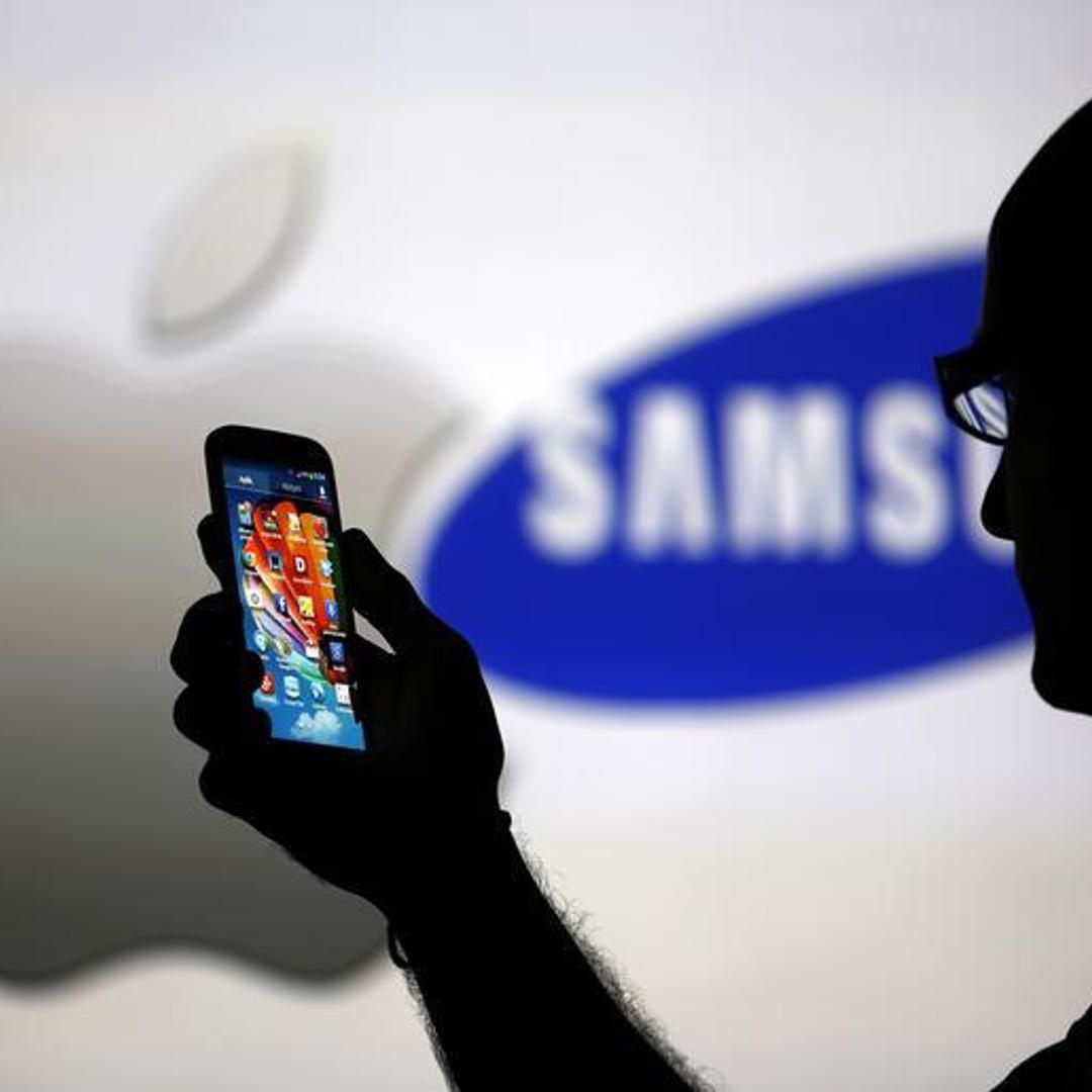 A man is silhouetted against a video screen with Apple and Samsung logos as he poses with a Samsung Galaxy S4 in this photo illustration taken in the central Bosnian town of Zenica