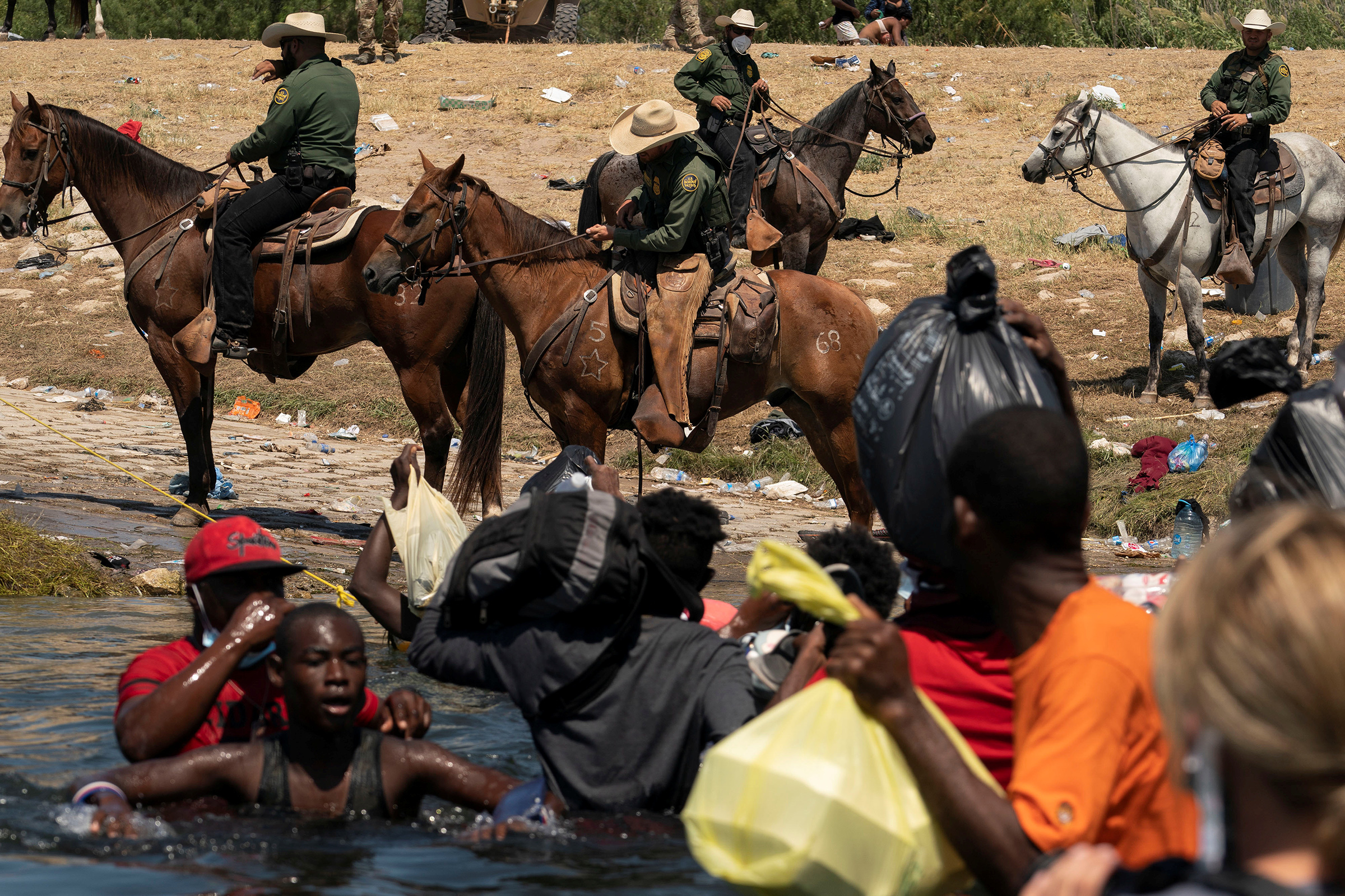 U.S. Border Patrol agents are seen on horseback on the U.S. side of the bank in Del Rio, Texas, as migrants seeking asylum attempt to cross the Rio Grande river into the U.S. after obtaining food and supplies in Mexico, as seen from Ciudad Acuna, Mexico,