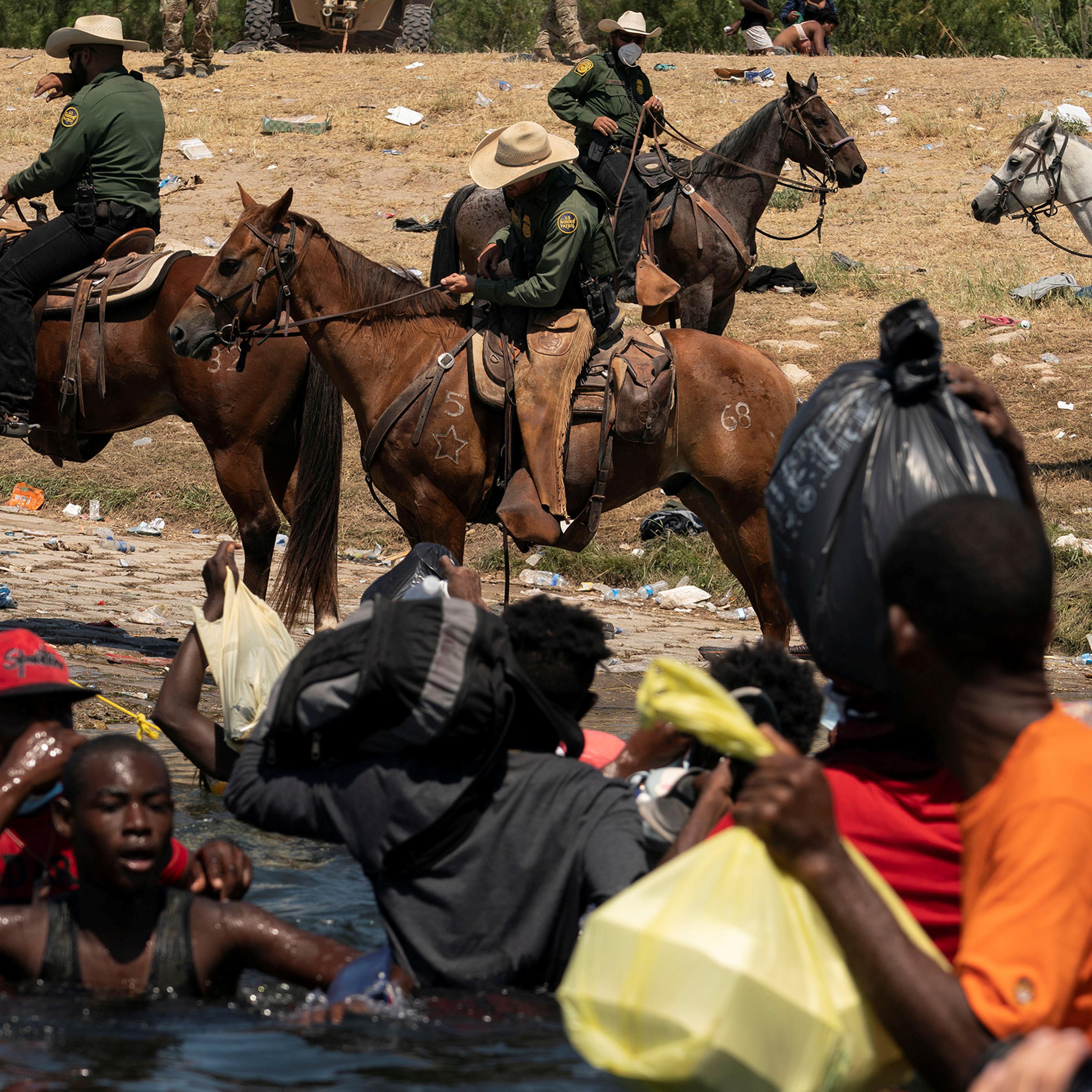 U.S. Border Patrol agents are seen on horseback on the U.S. side of the bank in Del Rio, Texas, as migrants seeking asylum attempt to cross the Rio Grande river into the U.S. after obtaining food and supplies in Mexico, as seen from Ciudad Acuna, Mexico,