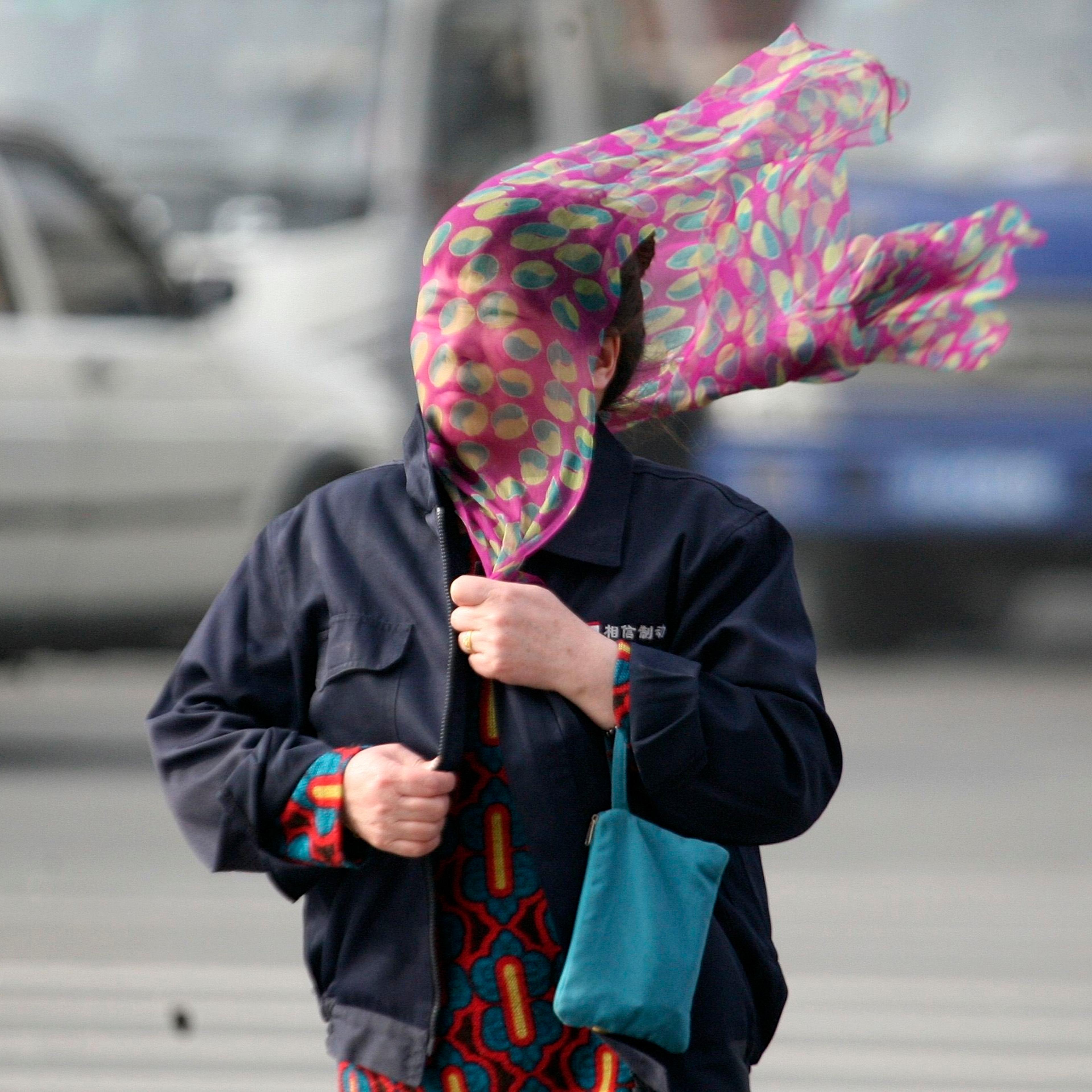 A woman covers her face with a scarf as she crosses a street amid strong wind in Shenyang