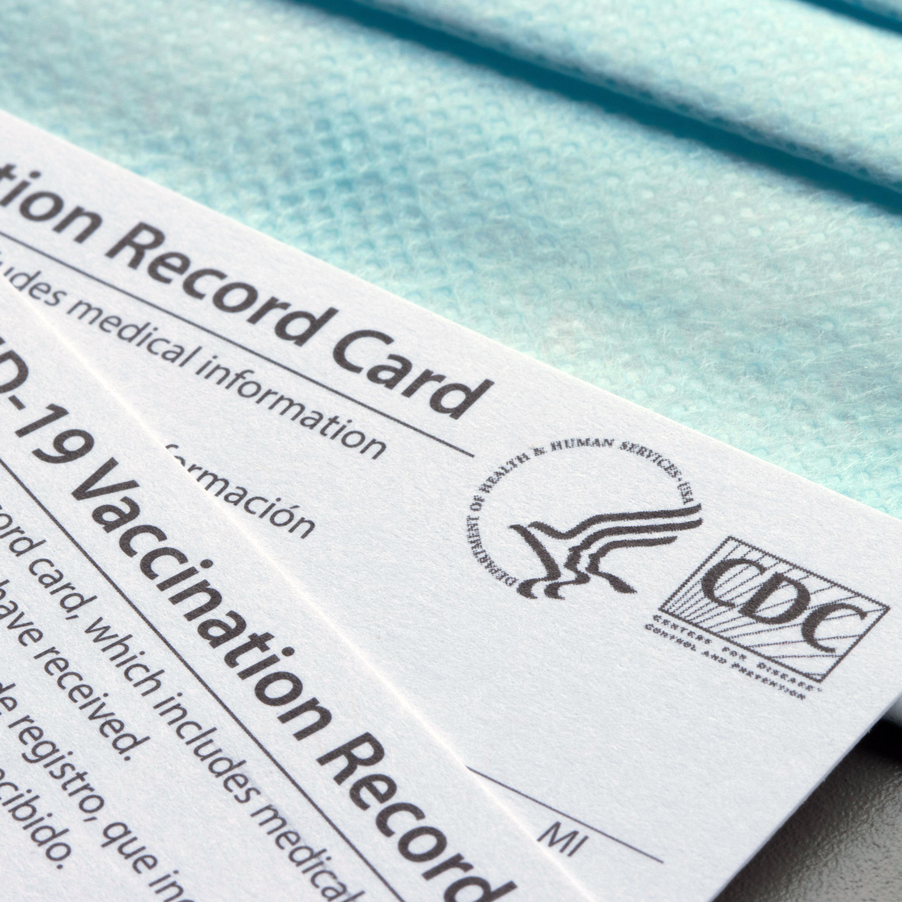 Closeup of Covid-19 Vaccination record cards issued by CDC (United States Centers for Disease Control and Prevention) on a blue disposable face mask.