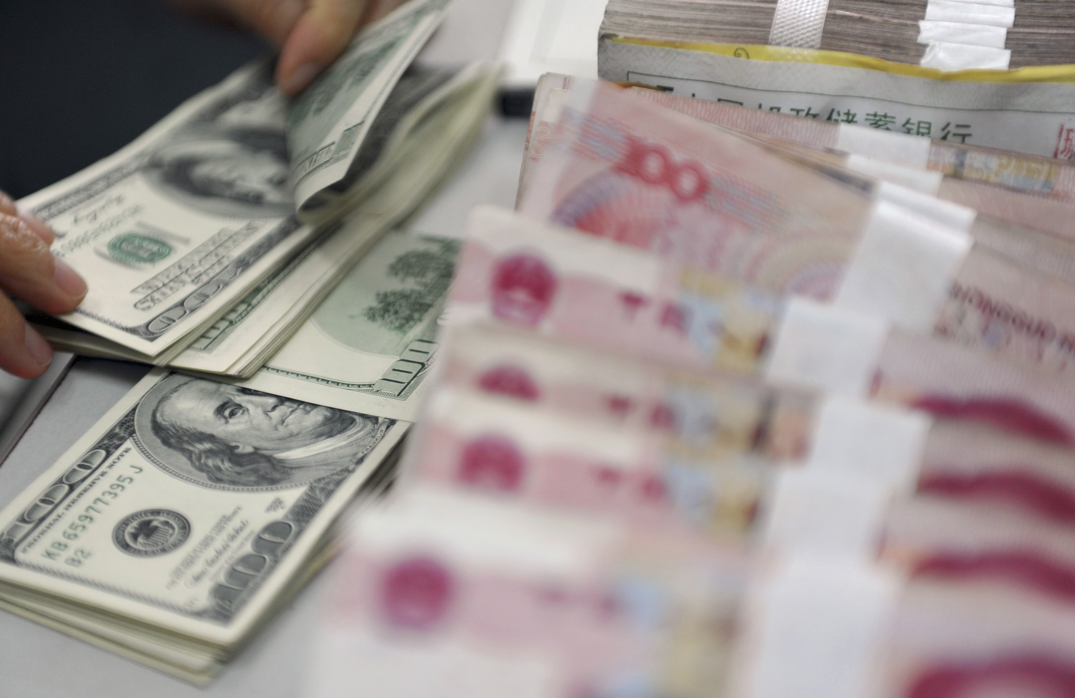 A clerk counts U.S. dollar banknotes after counting Chinese 100 Yuan banknotes at a branch of the Agricultural Bank of China in Qionghai