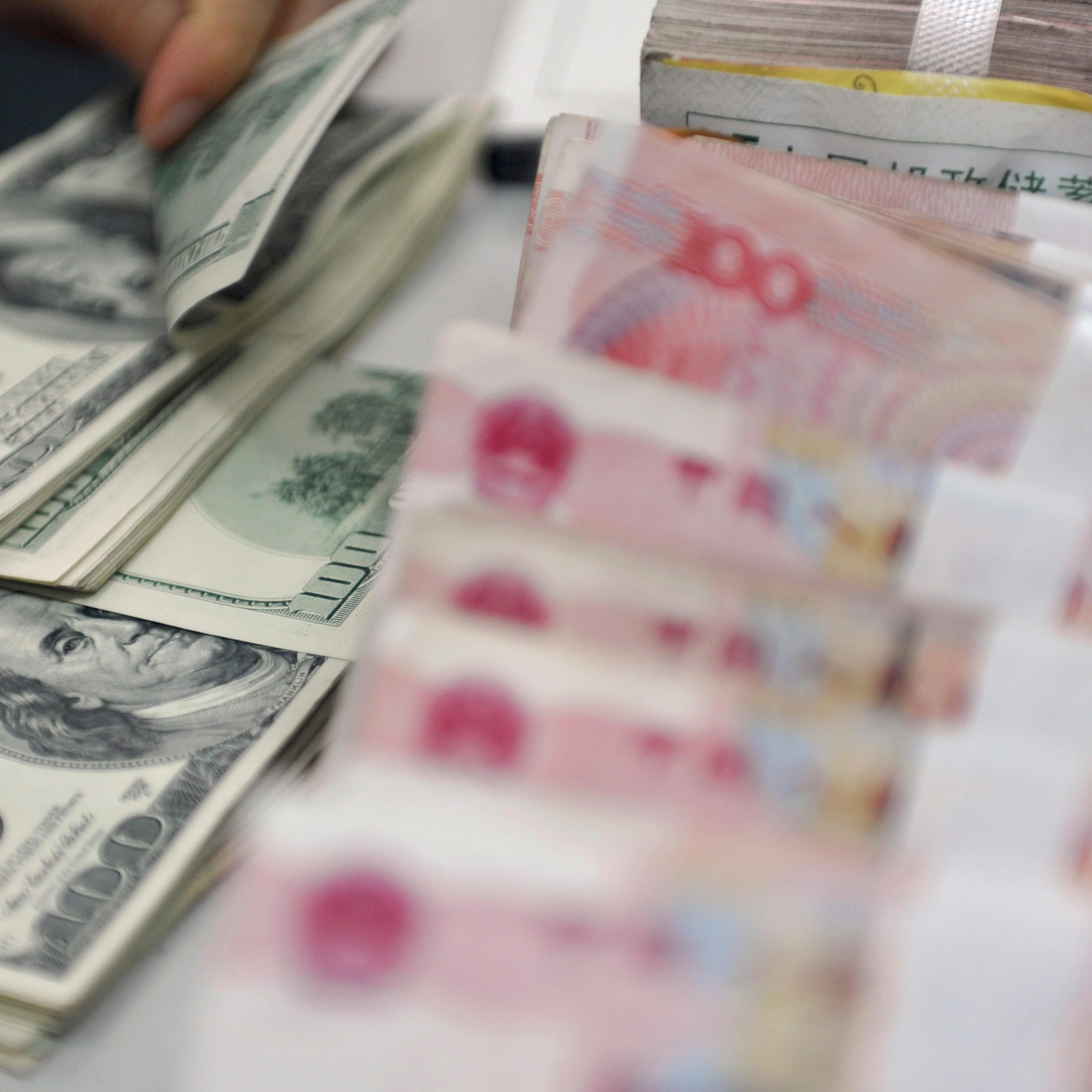 A clerk counts U.S. dollar banknotes after counting Chinese 100 Yuan banknotes at a branch of the Agricultural Bank of China in Qionghai