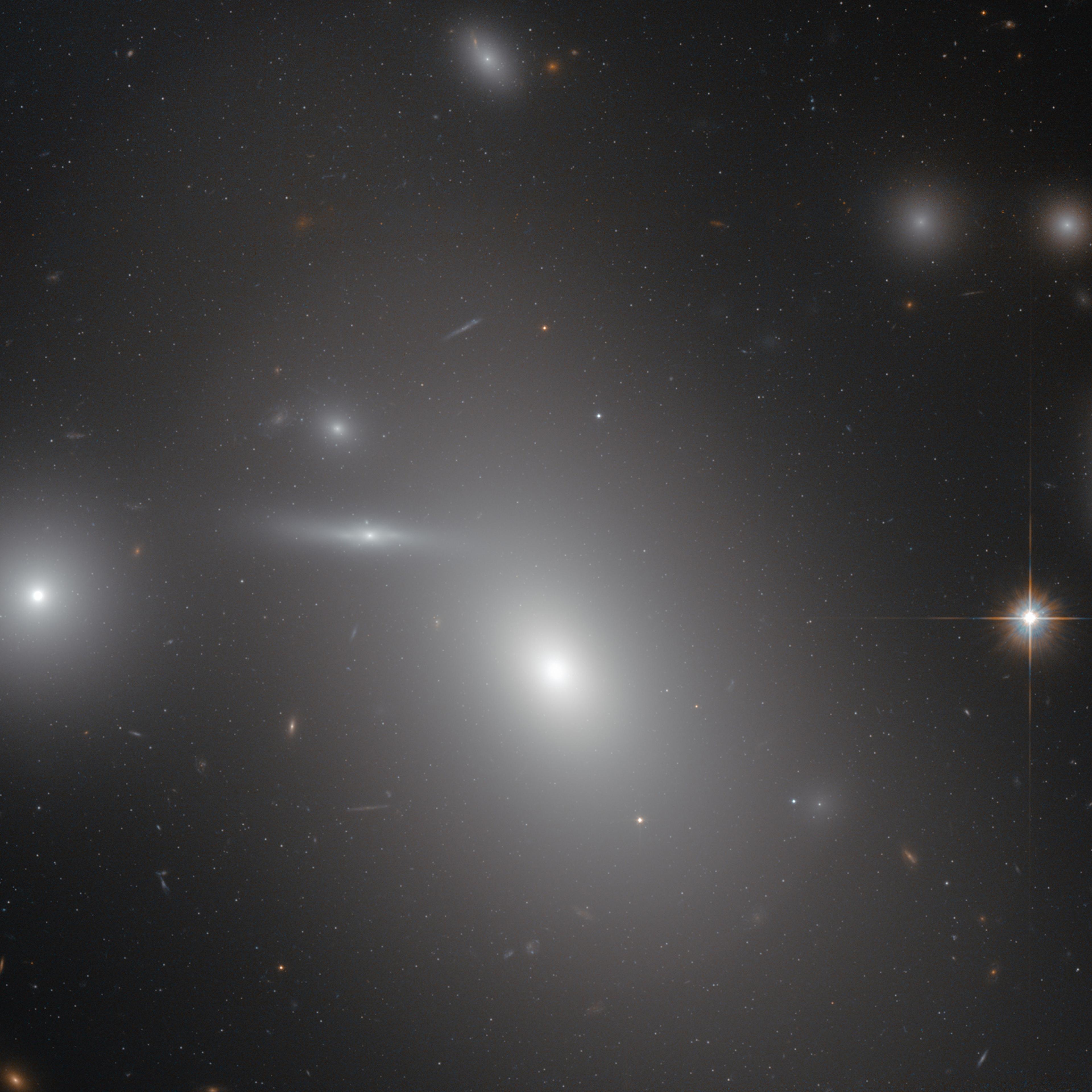 The elliptical galaxy NGC 4889 in front of hundreds of background galaxies, and deeply embedded within the Coma galaxy cluster. Hidden from human eyes, is a gigantic supermassive black hole at the centre of the galaxy.