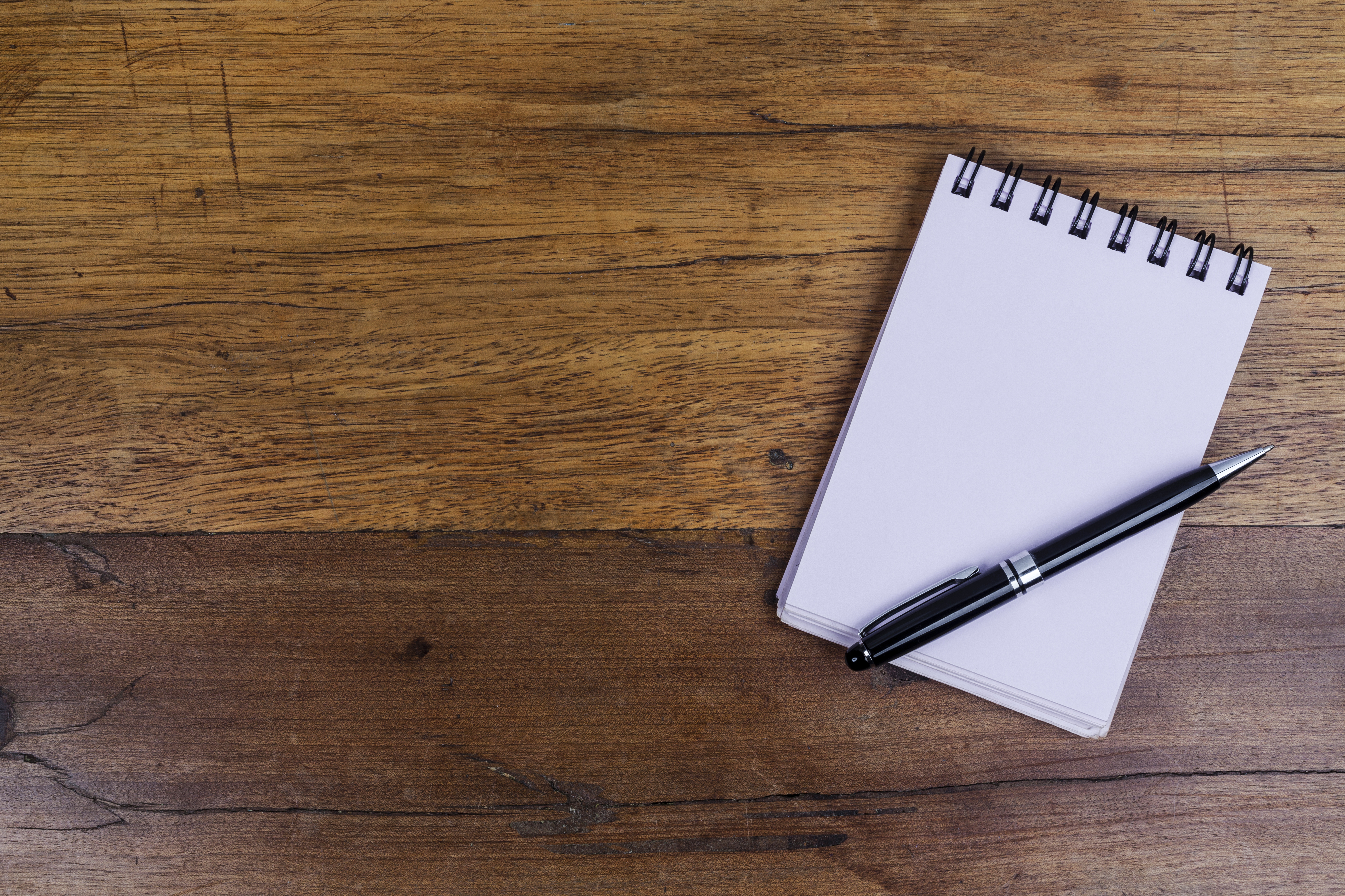 Notebook on right side of wooden table with pen on