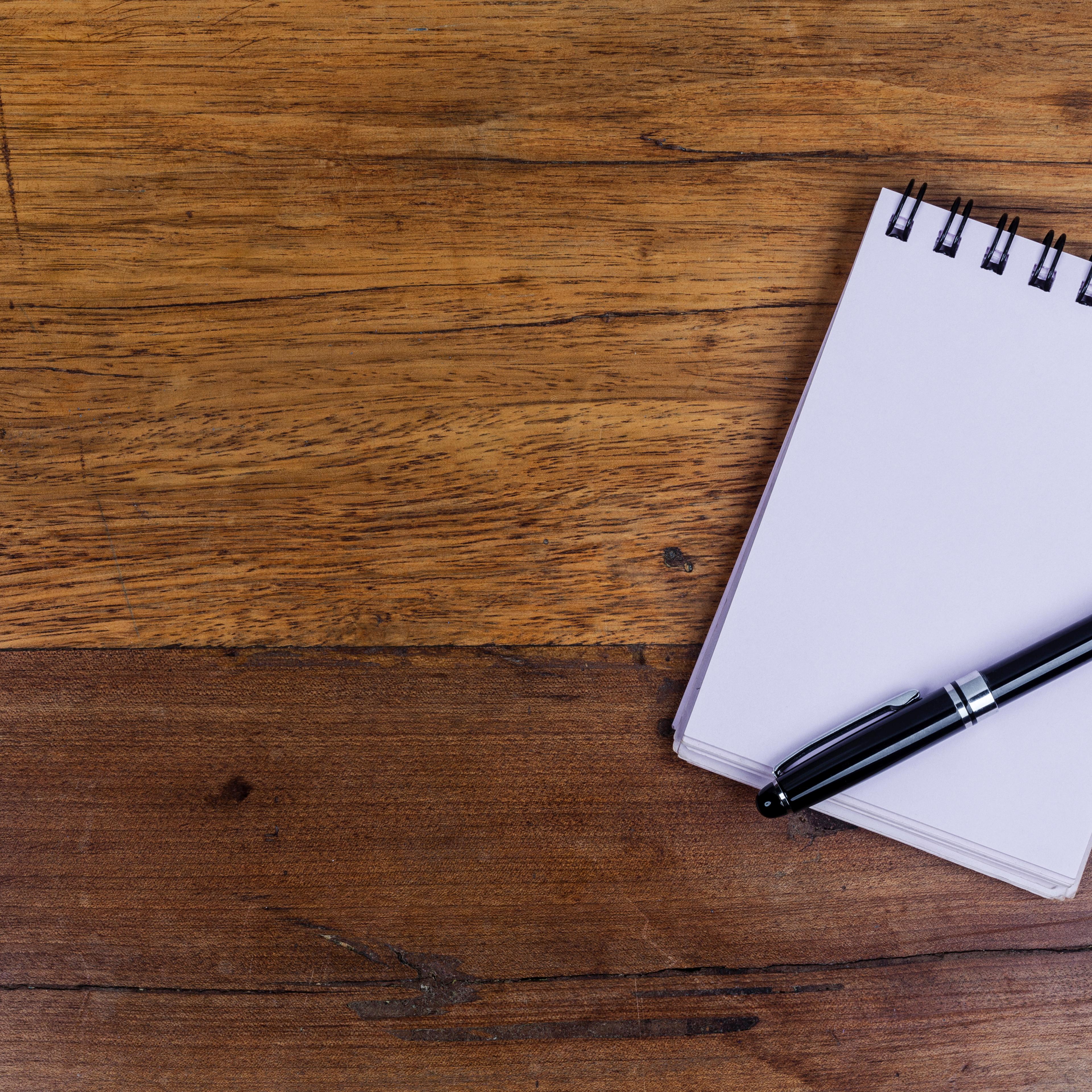 Notebook on right side of wooden table with pen on