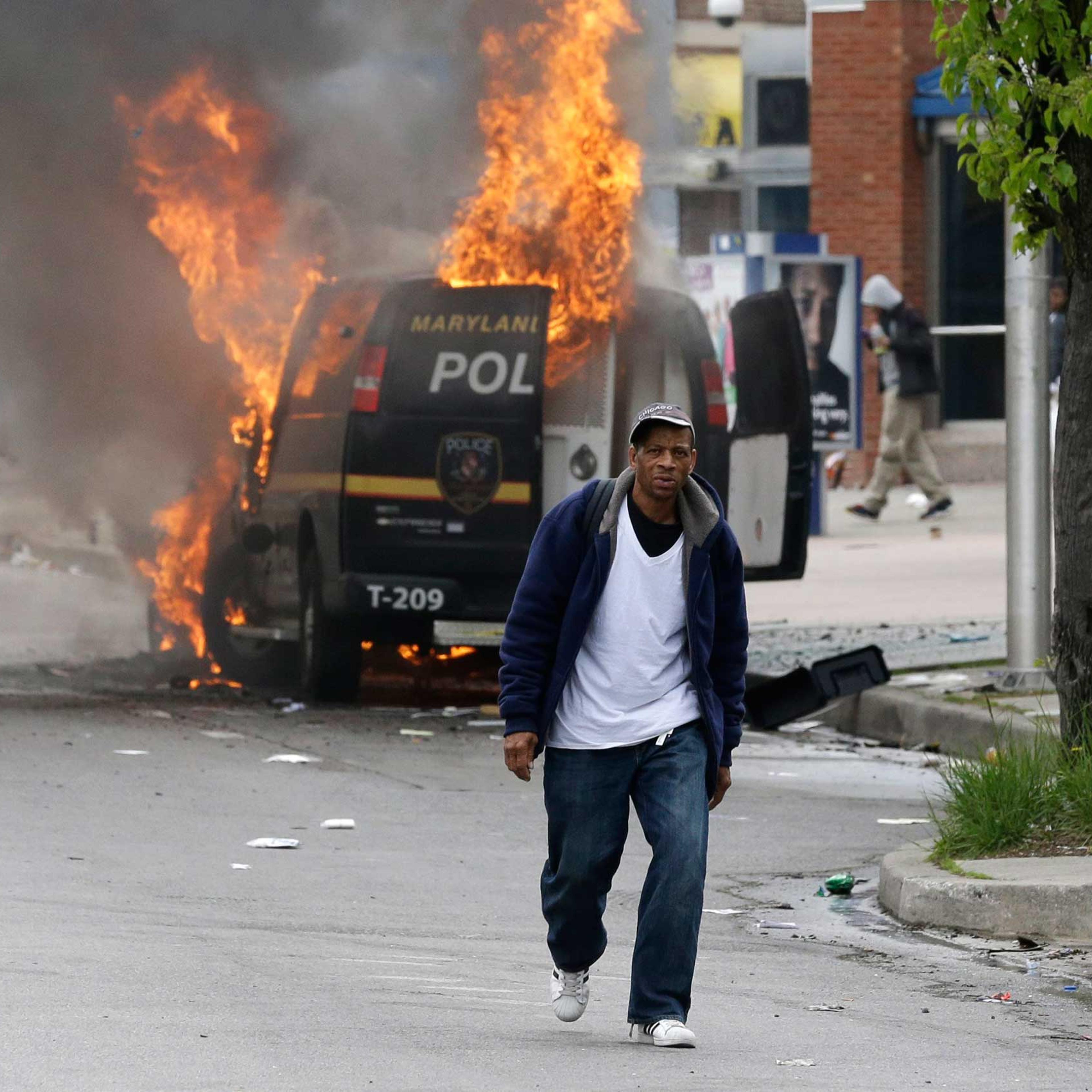 A man walks past a burning police vehicle in Baltimore on April 27, 2015.