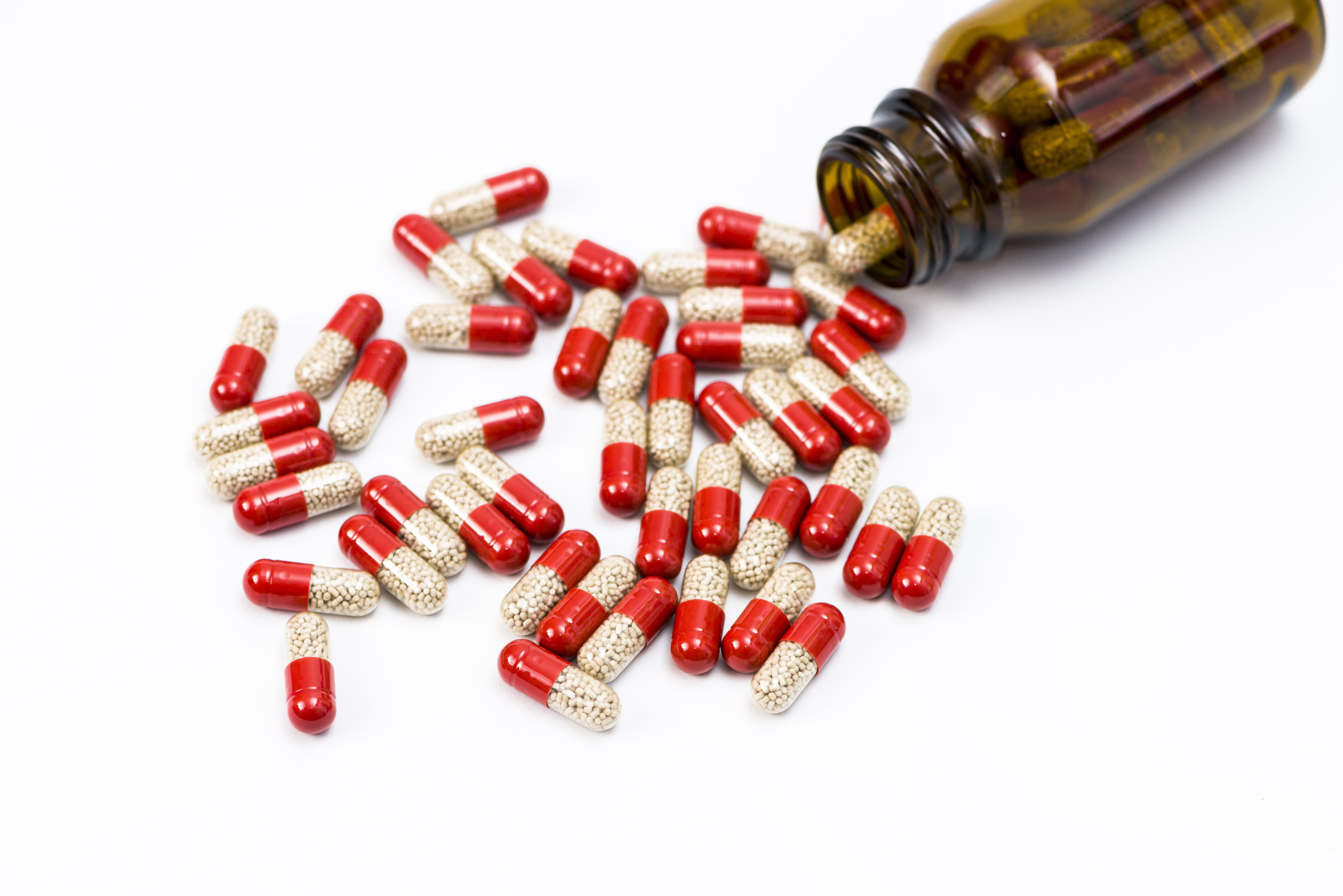 Many red and transparent medical capsules, filled with yellow medicine, pouring out of a brown bottle, displayed on a white table n Wuerzburg, Bavaria, Germany in December 2014.