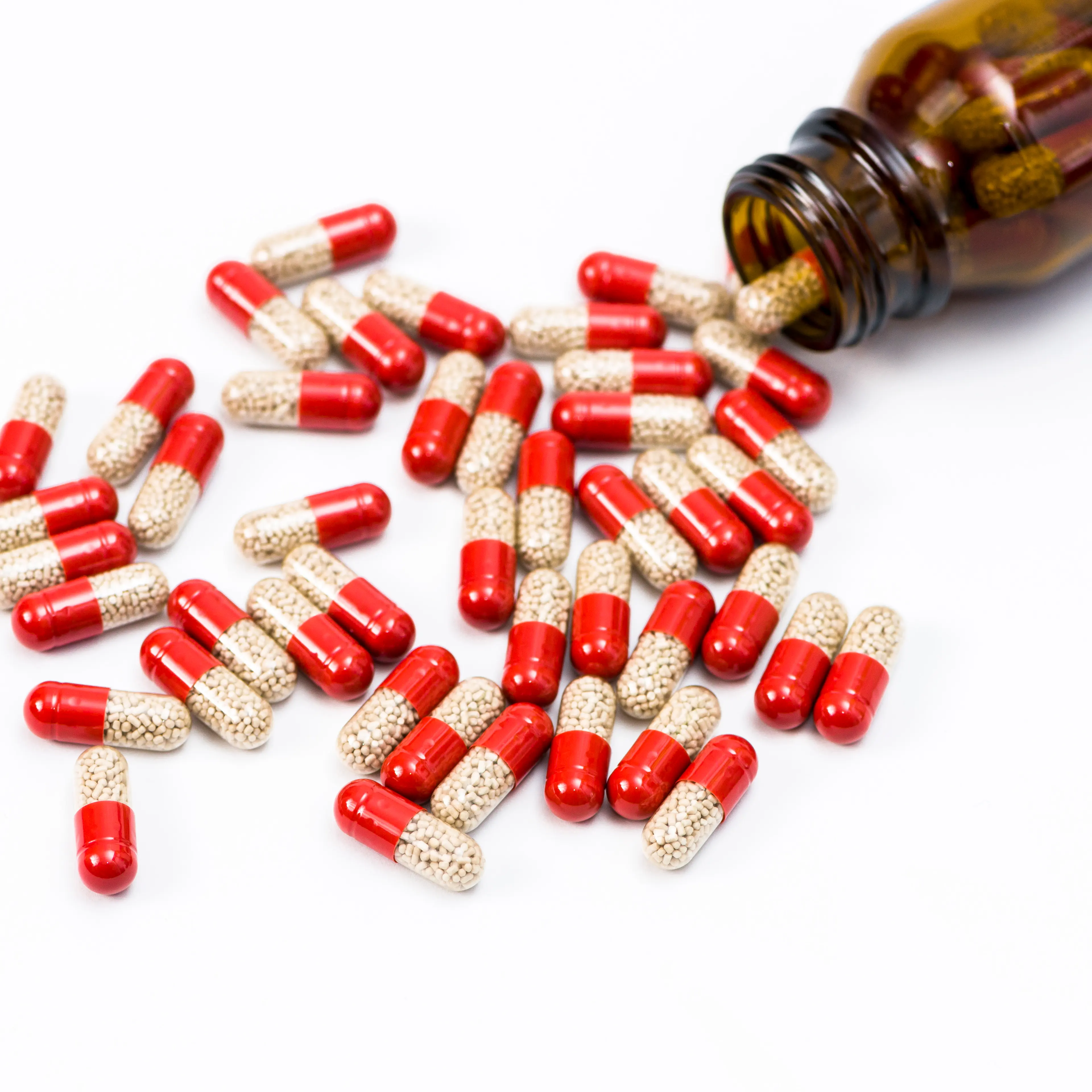Many red and transparent medical capsules, filled with yellow medicine, pouring out of a brown bottle, displayed on a white table n Wuerzburg, Bavaria, Germany in December 2014.