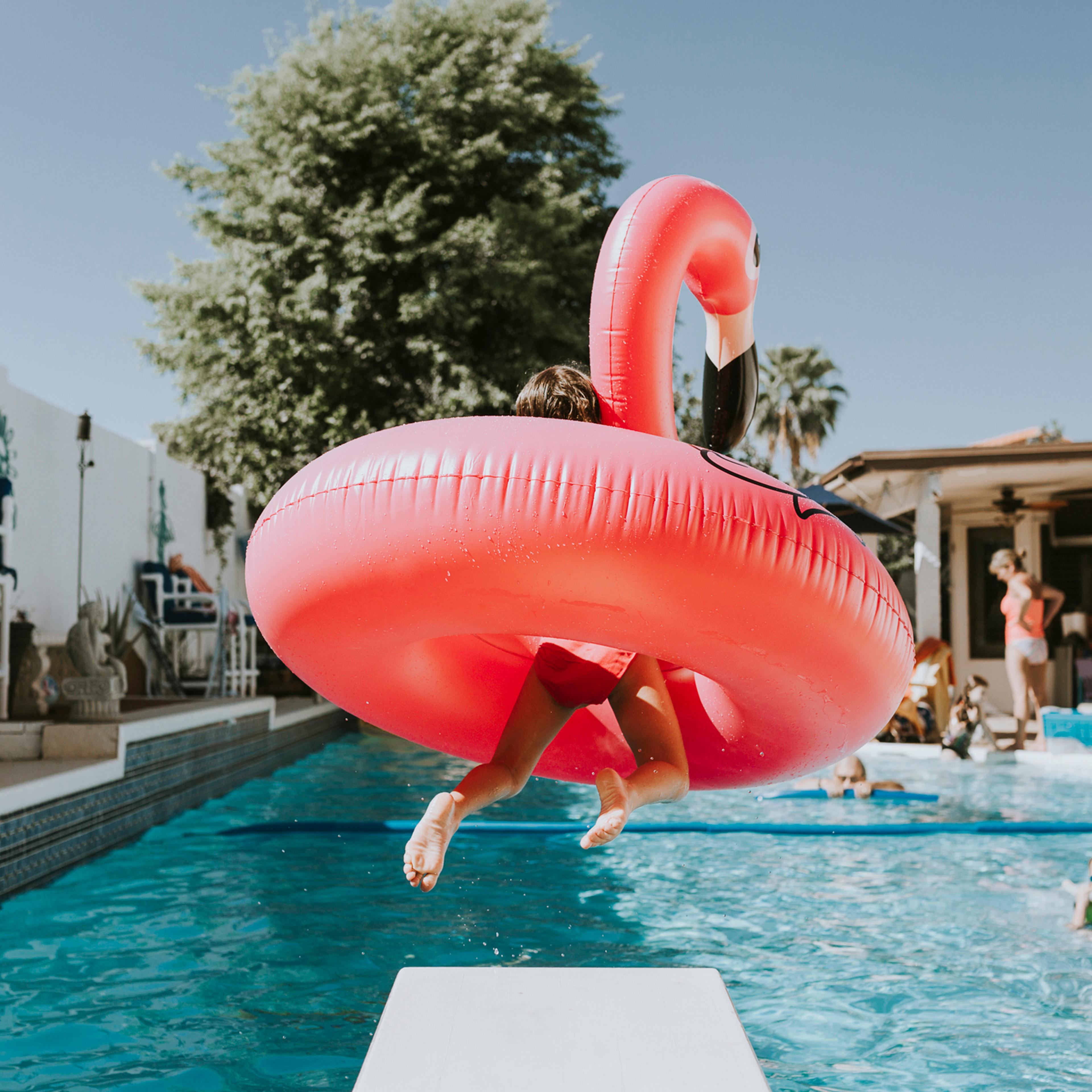 Girl jumping into swimming pool with pink flamingo