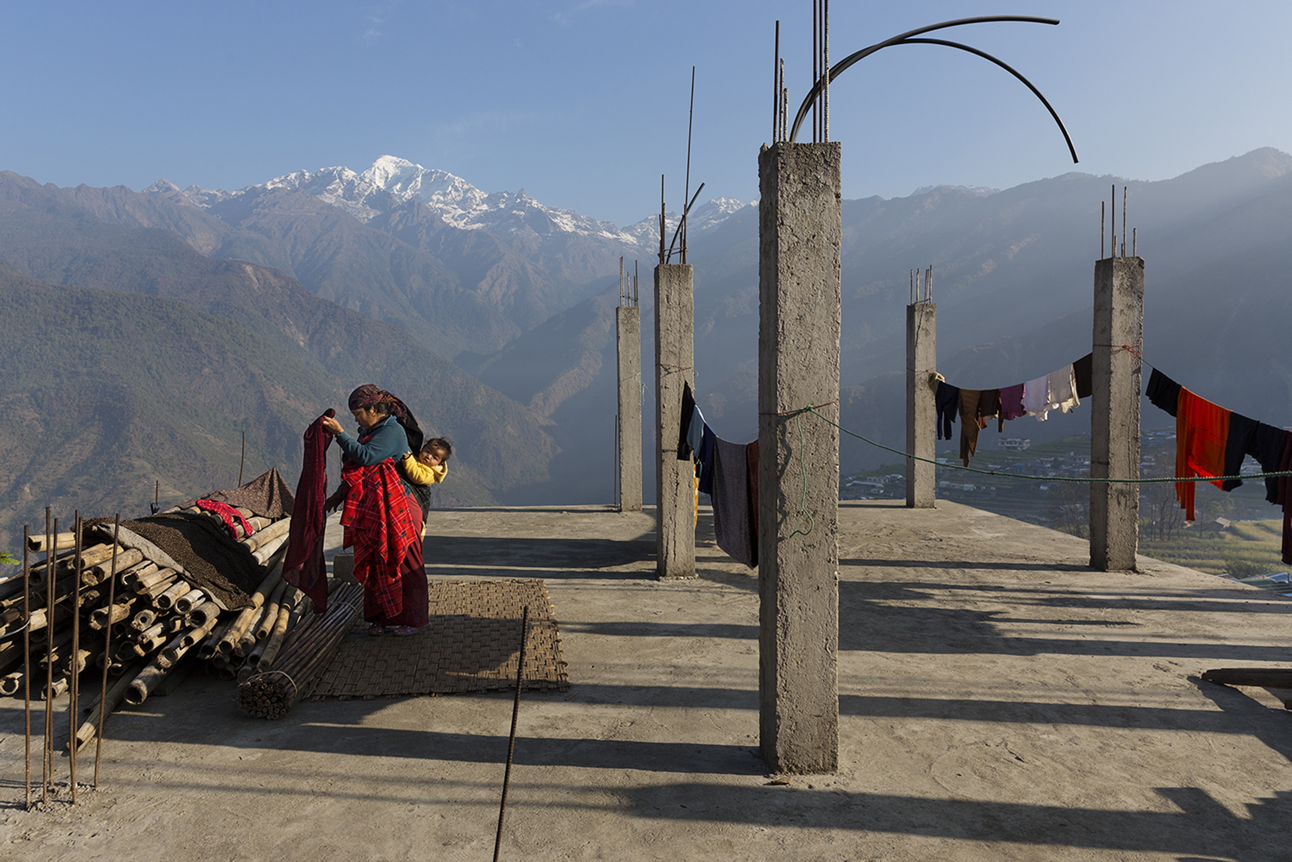 A woman hangs laundry with the Buddha Himal mountain behind her in the Himalyan village of Barpak, in Gorkha district, Nepal. Though international donors stepped up to provide aid in the aftermath of the 2015 quakes, money for rebuilding homes has yet to