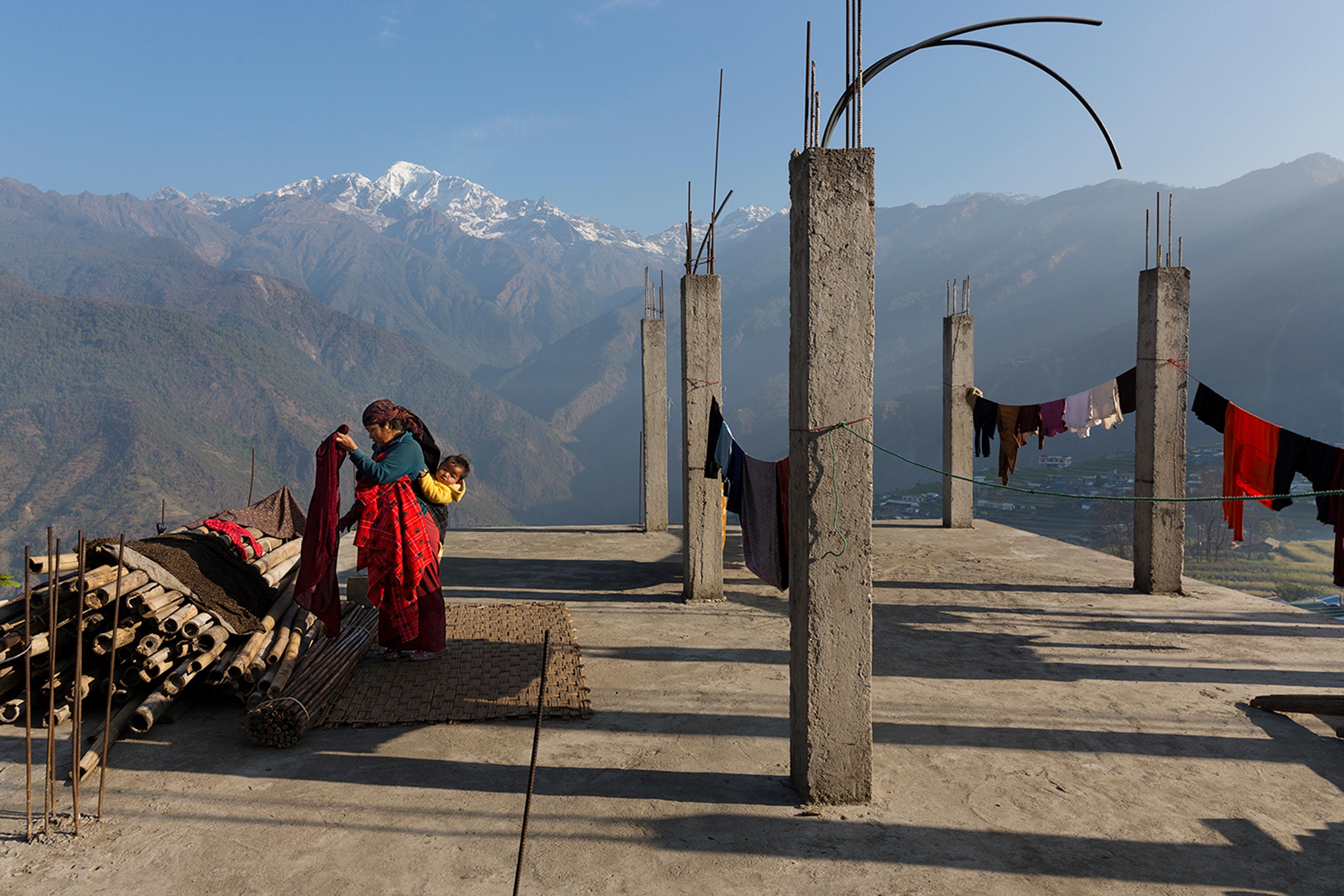 A woman hangs laundry with the Buddha Himal mountain behind her in the Himalyan village of Barpak, in Gorkha district, Nepal. Though international donors stepped up to provide aid in the aftermath of the 2015 quakes, money for rebuilding homes has yet to