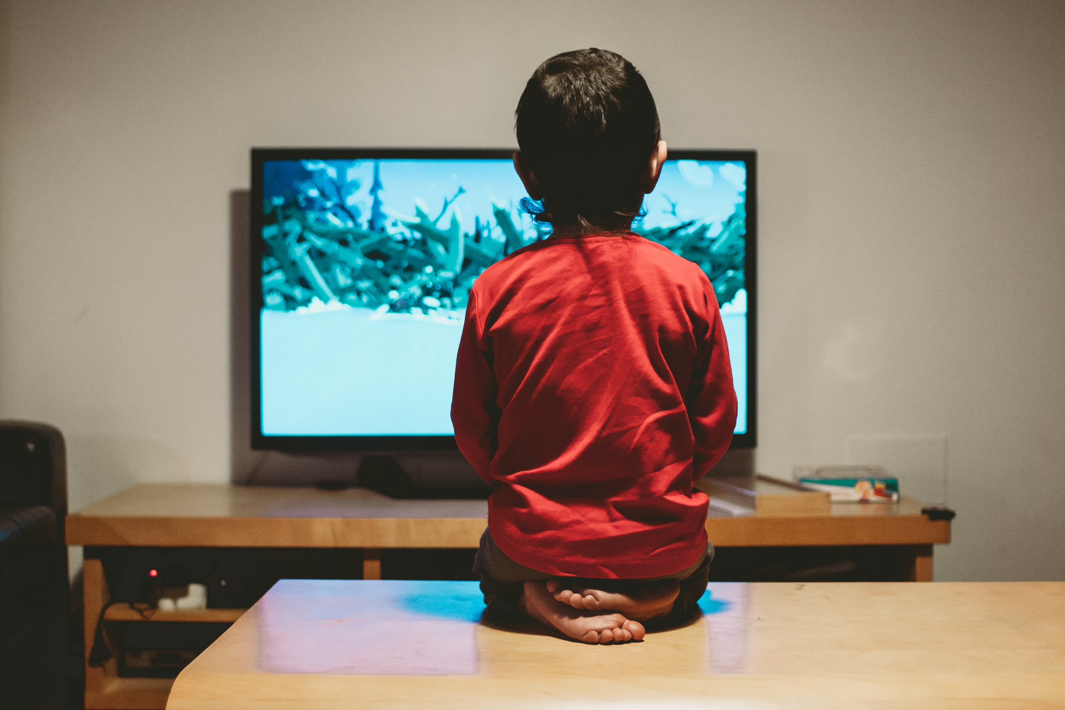 rear view of a boy sitting on the coffee table looking at the tv
