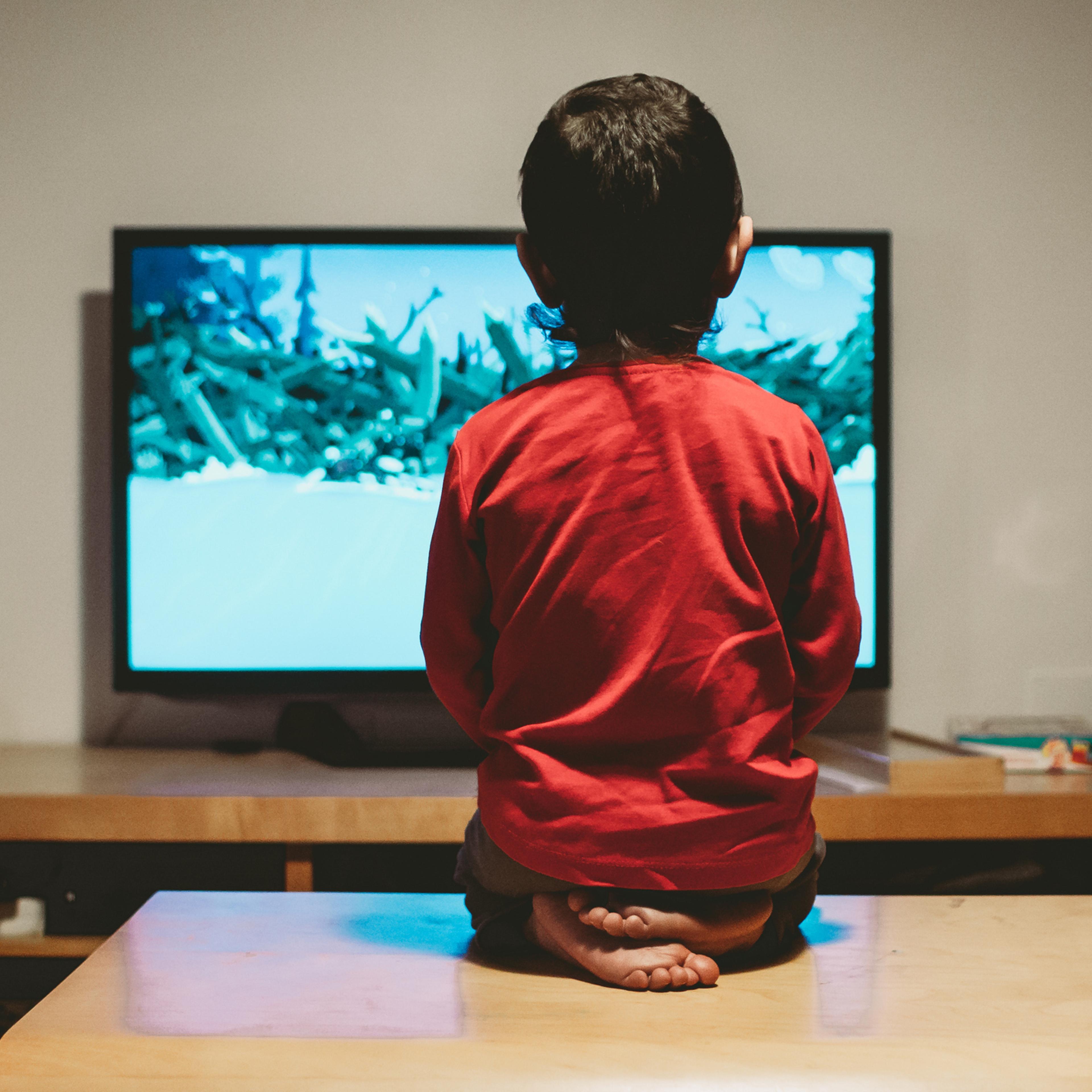 rear view of a boy sitting on the coffee table looking at the tv