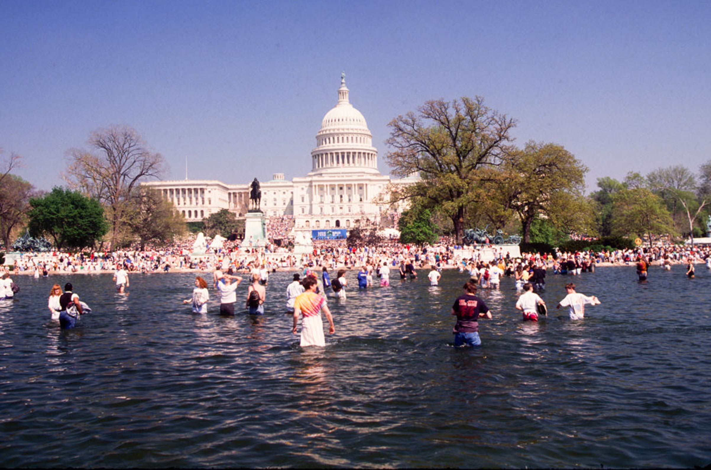View of the crowd gathering for an Earth Day rally on the U.S. Capitol grounds, some in the Capitol Reflecting Pool on April 22, 1990, in Washington D.C.