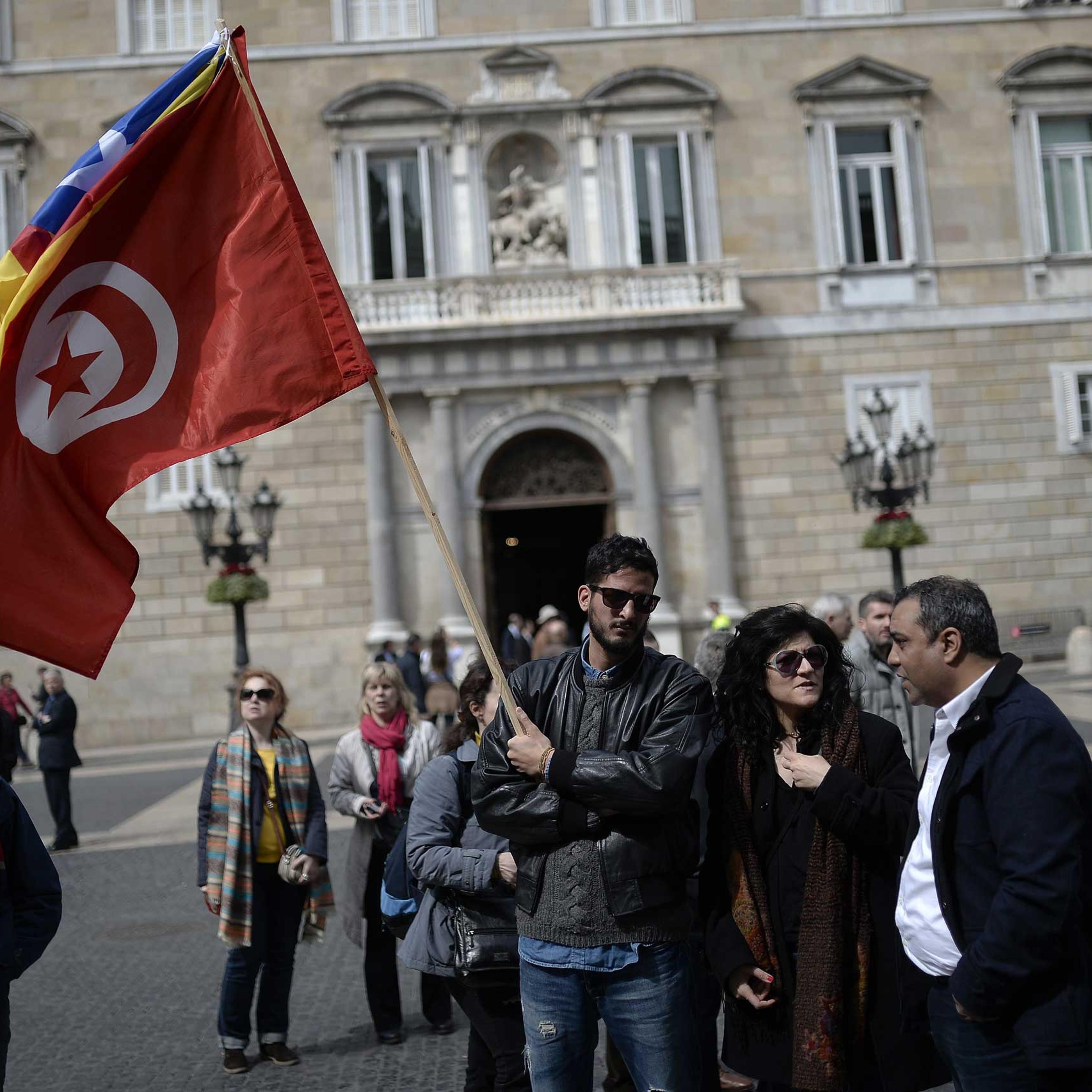A man holds a Tunisian and a Catalan flag during a minute of silence held outside Barcelona's city hall in Barcelona on March 19, 2015.
