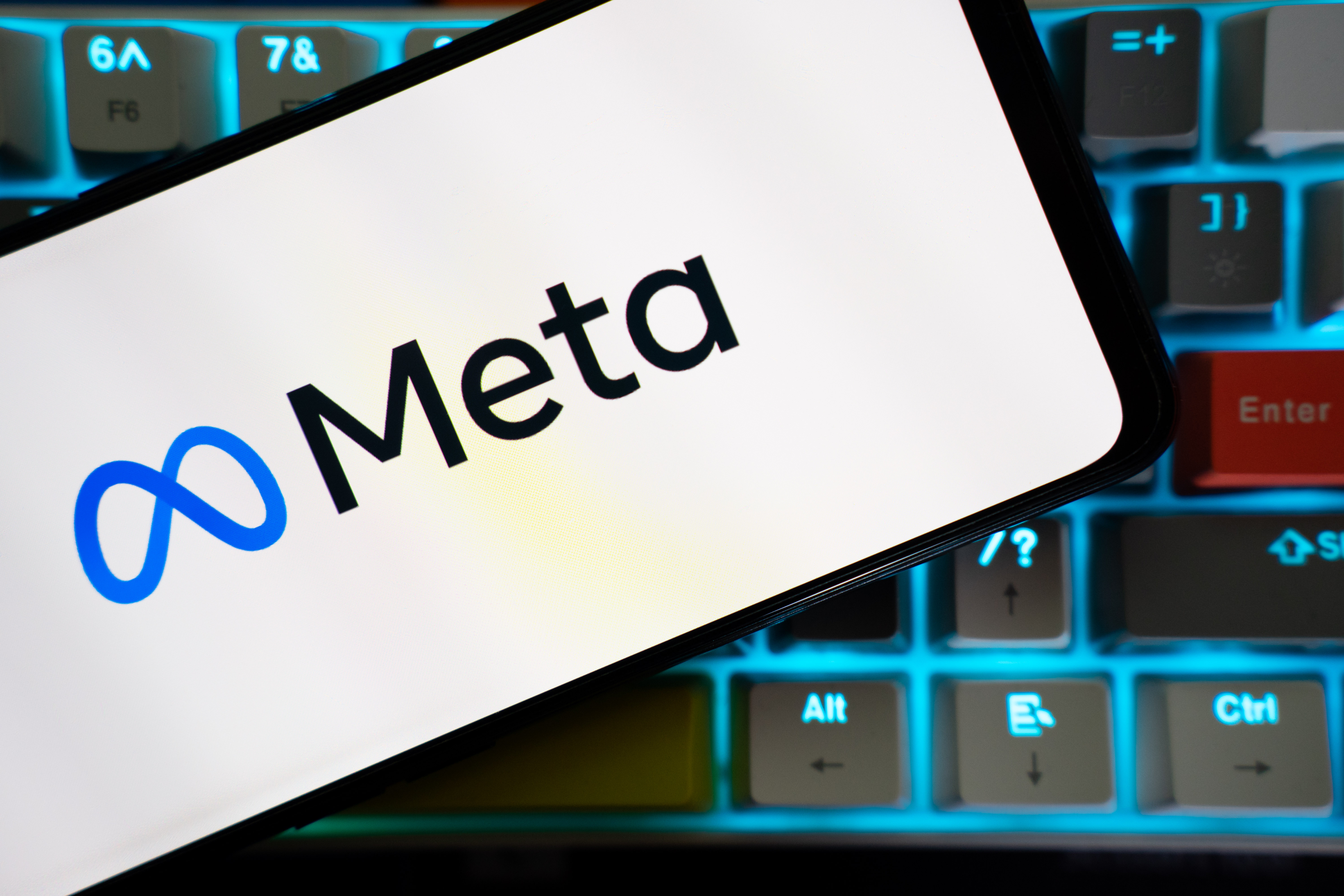A mobile phone over a keyboard is seen, with the logo of Meta on its screen.