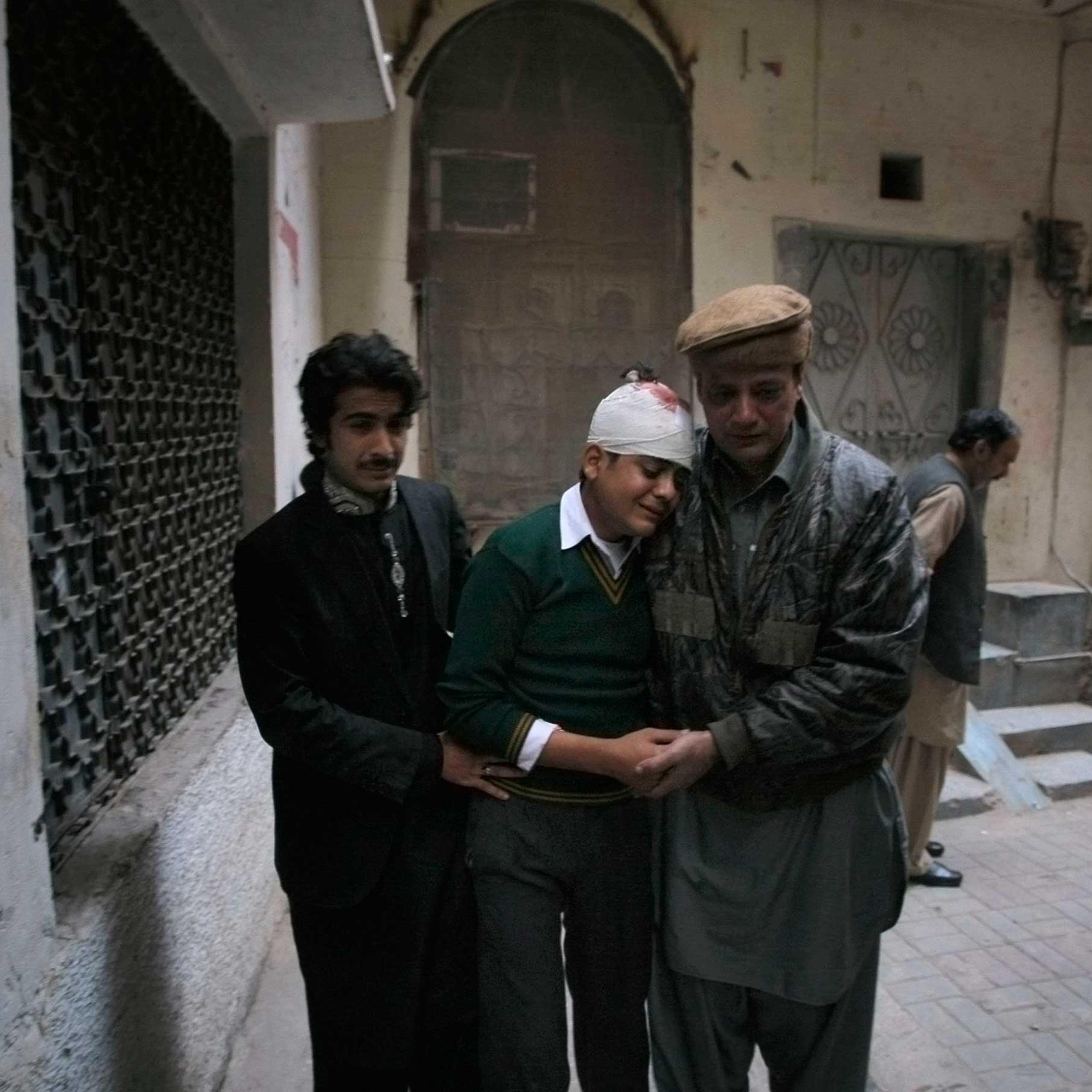 The uncle and cousin of injured student Mohammad Baqair, center, comfort him as he mourns the death of his mother who was a teacher at the school which was attacked by Taliban, in Peshawar, Pakistan, Tuesday, Dec. 16, 2014.