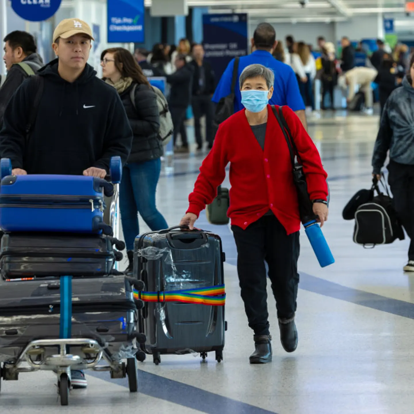 Travelers at LAX airport, including a woman wearing a mask.
