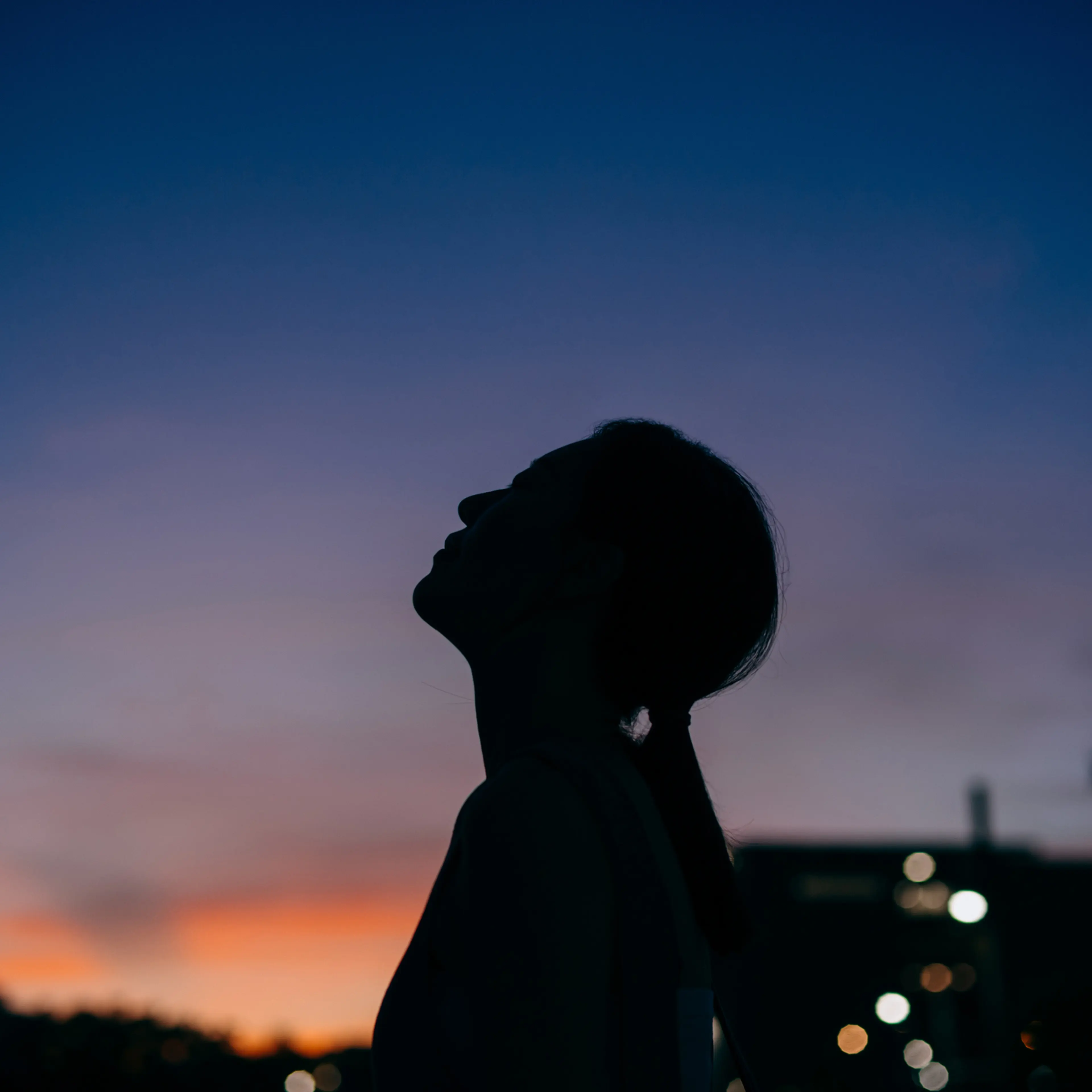 Silhouette of the side profile of young Asian woman looking over sky enjoying twilight in the nature. Freedom in nature. Connection with nature