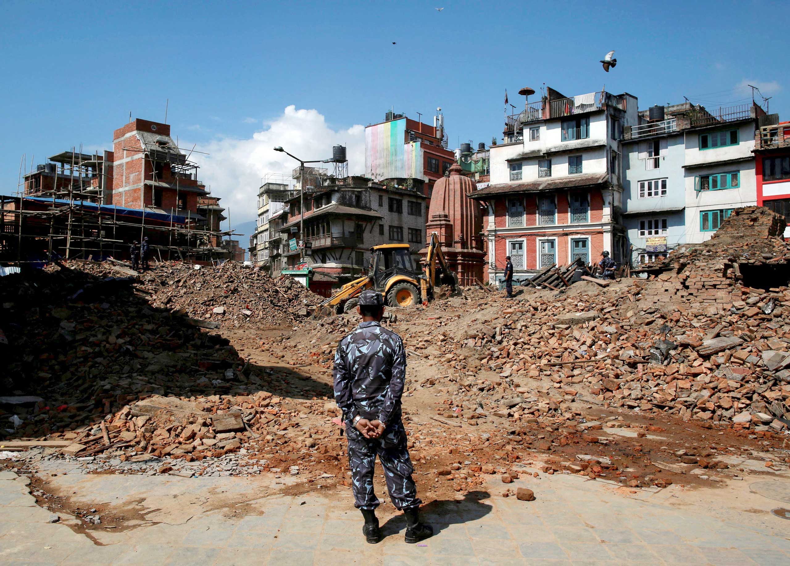 A member of the Nepalese police looks on as an excavator is used to dig through rubble to search for bodies, in the aftermath of Saturday's earthquake in Kathmandu, Nepal, April 27, 2015.