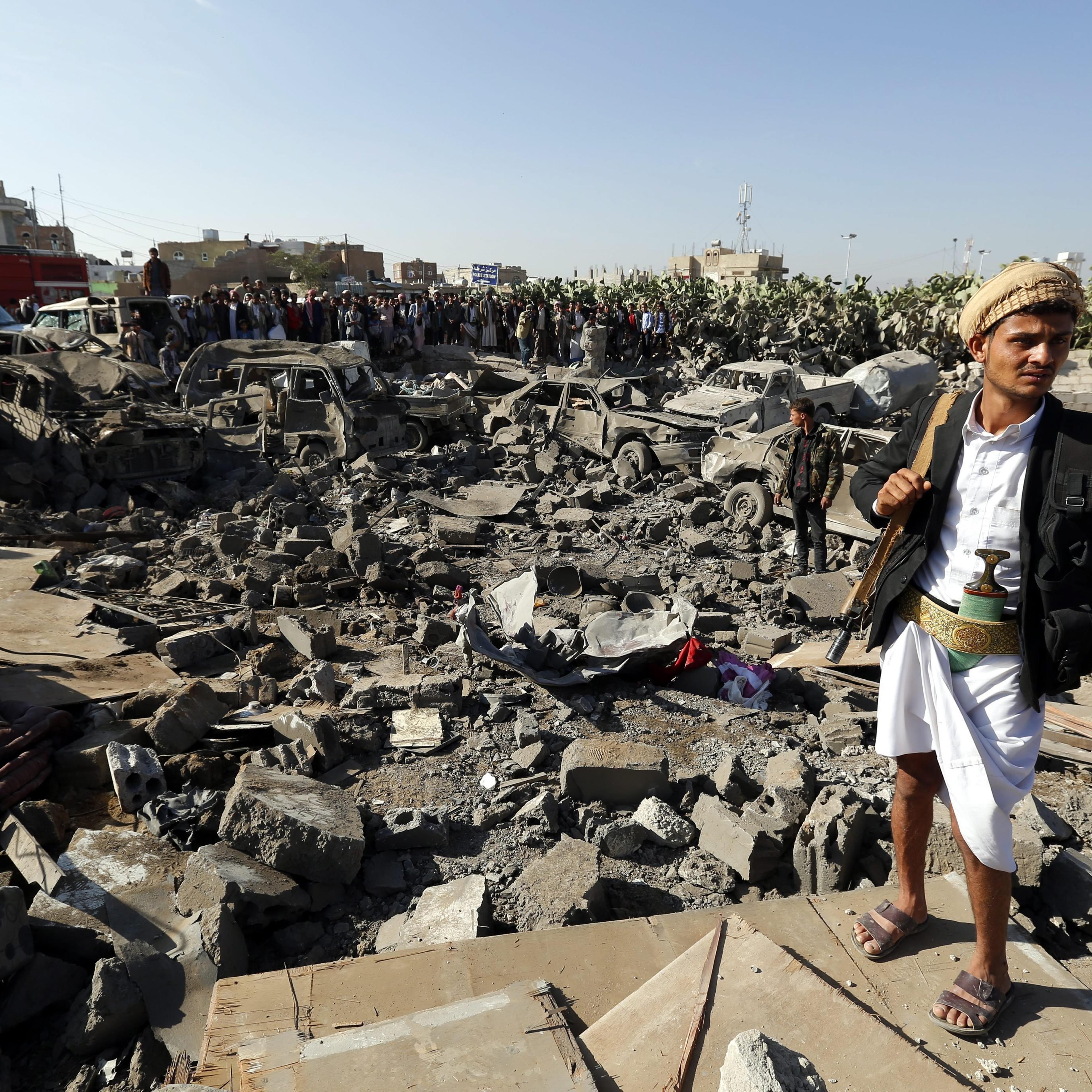 An armed member of Houthi militia (R) keeps watch as people gather beside vehicles which were allegedly destroyed by a Saudi air strike, in Sana'a, Yemen on March 26, 2015.