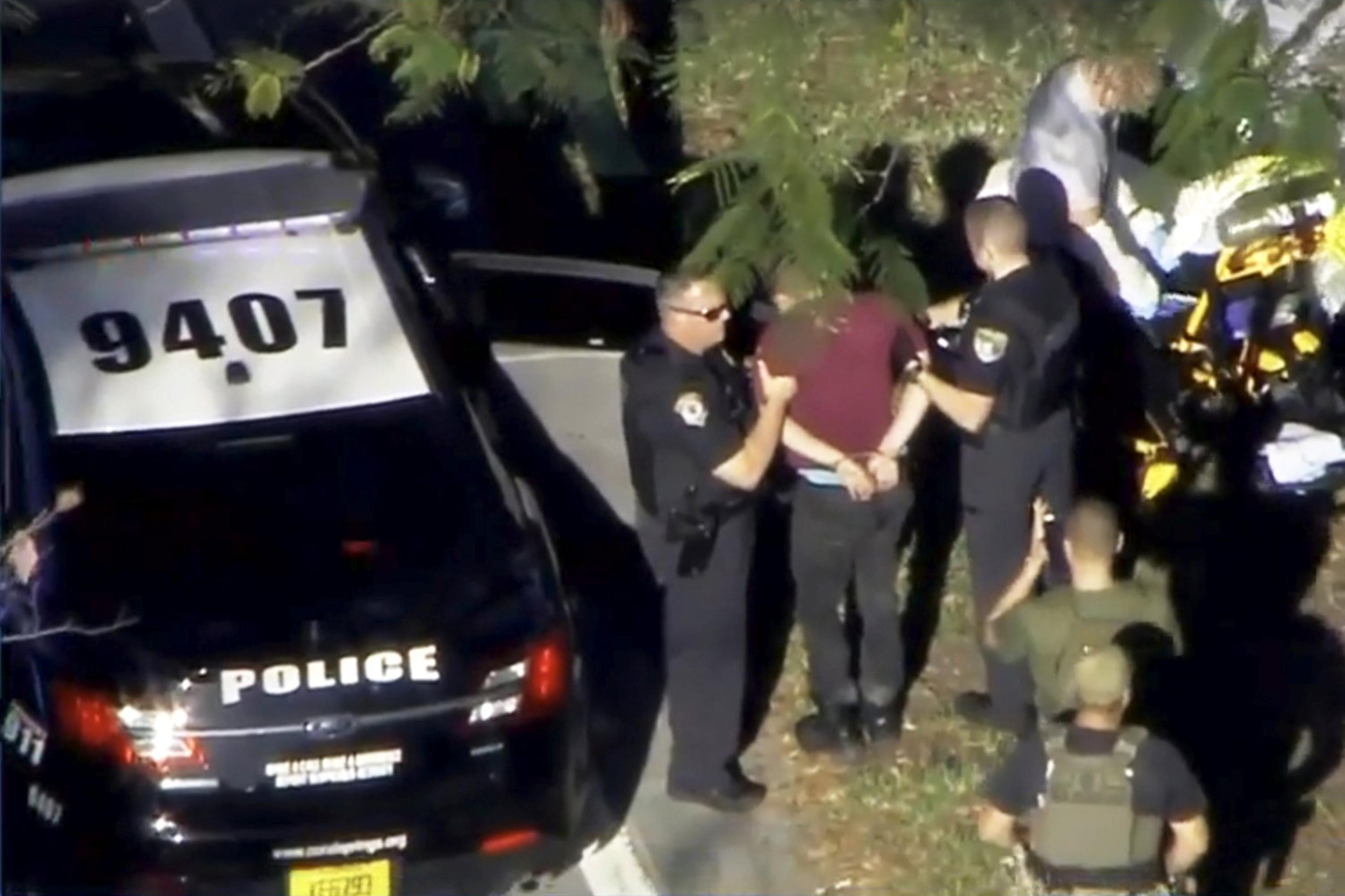 A man placed in handcuffs is led by police near Marjory Stoneman Douglas High School following a shooting incident in Parkland