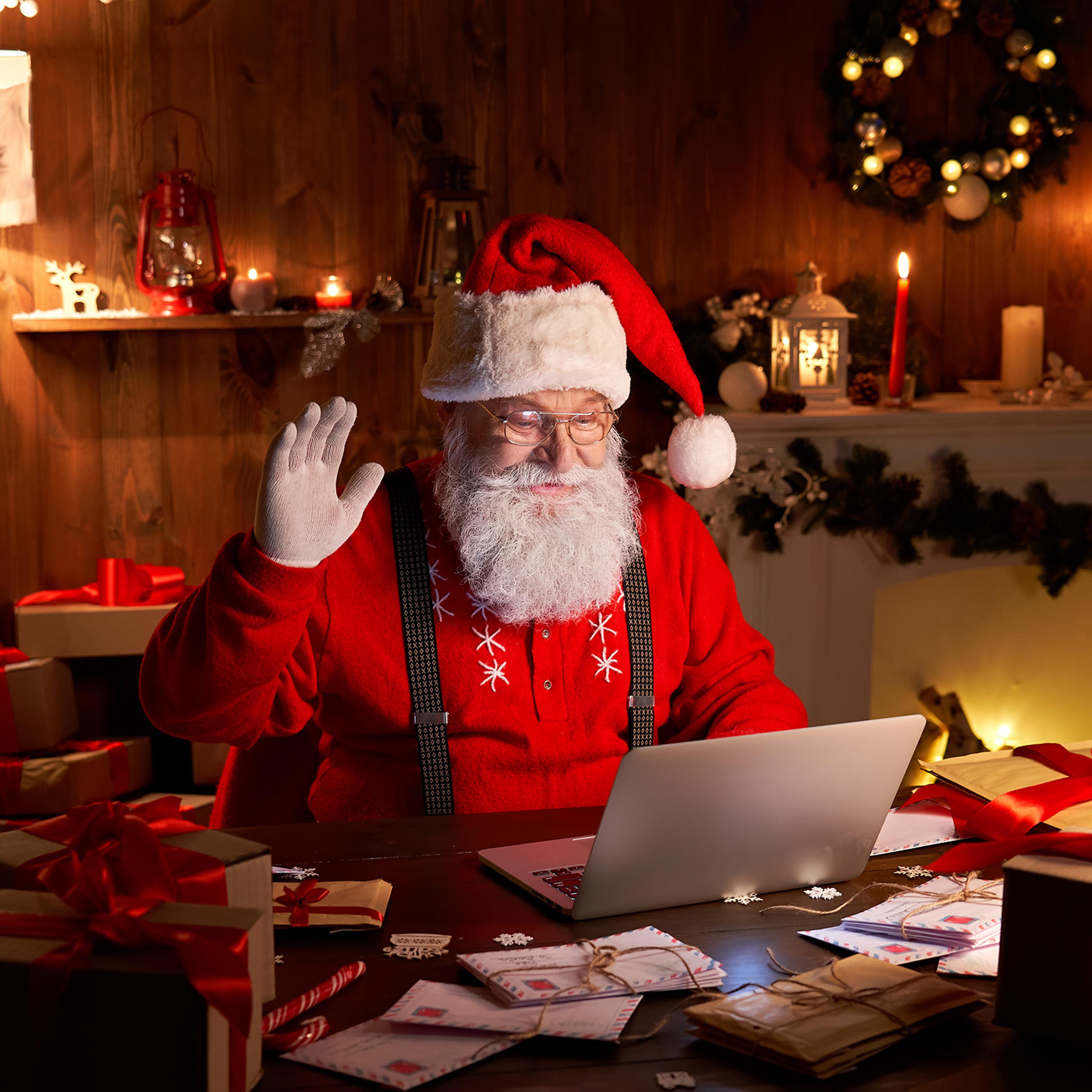 Happy Santa Claus waving hand video calling kid talking to child greeting on Merry Christmas, Happy New Year in virtual video online chat on laptop sitting at home table late with present on xmas eve.