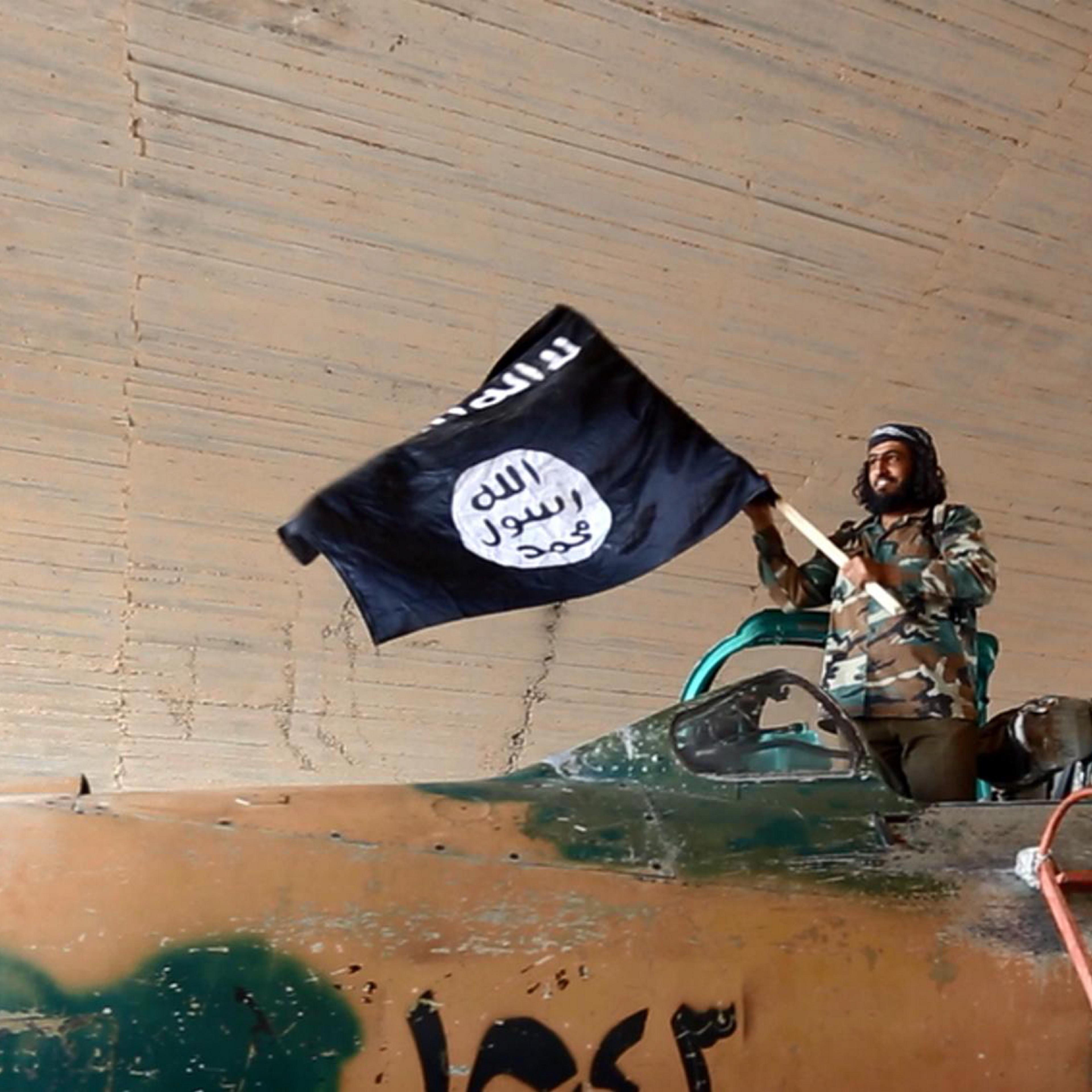 ISIS fighter waves a flag while standing on a captured government fighter jet in Raqqa, Syria, 2015.