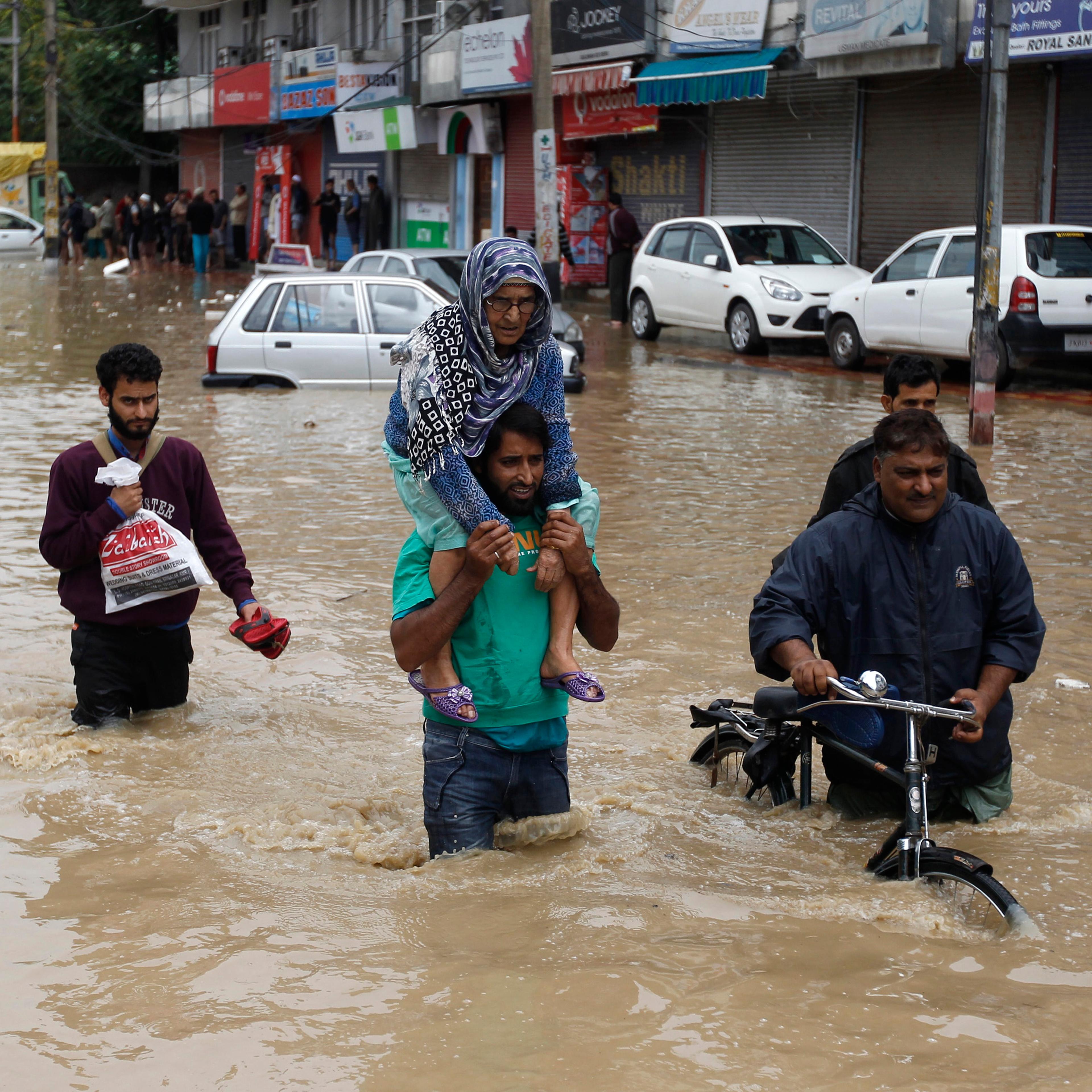 A Kashmiri man evacuates an elderly woman to a higher ground at a flooded road in Srinagar