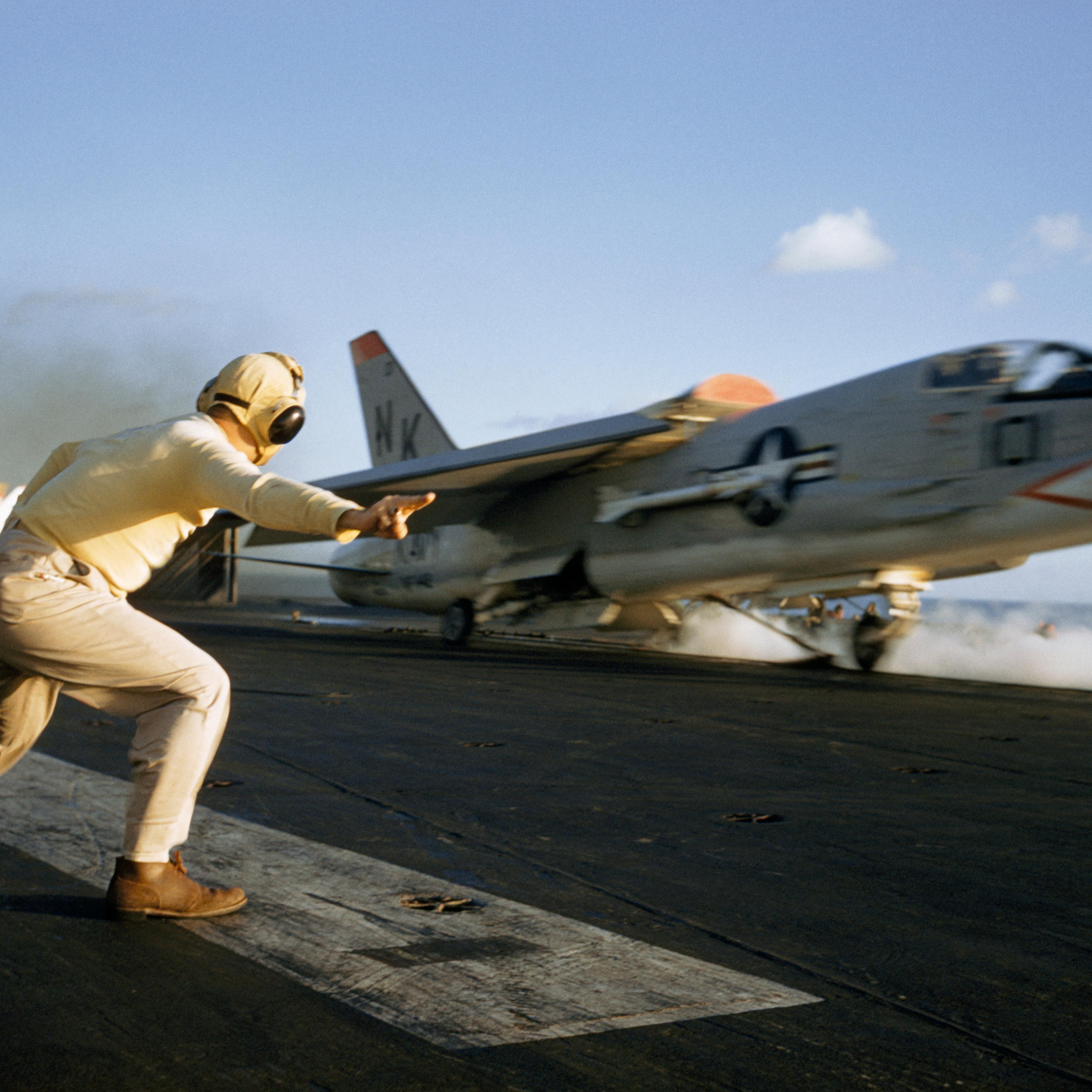 An officer guides a Crusader aircraft at launch on USS Ranger's deck, Pacific Ocean