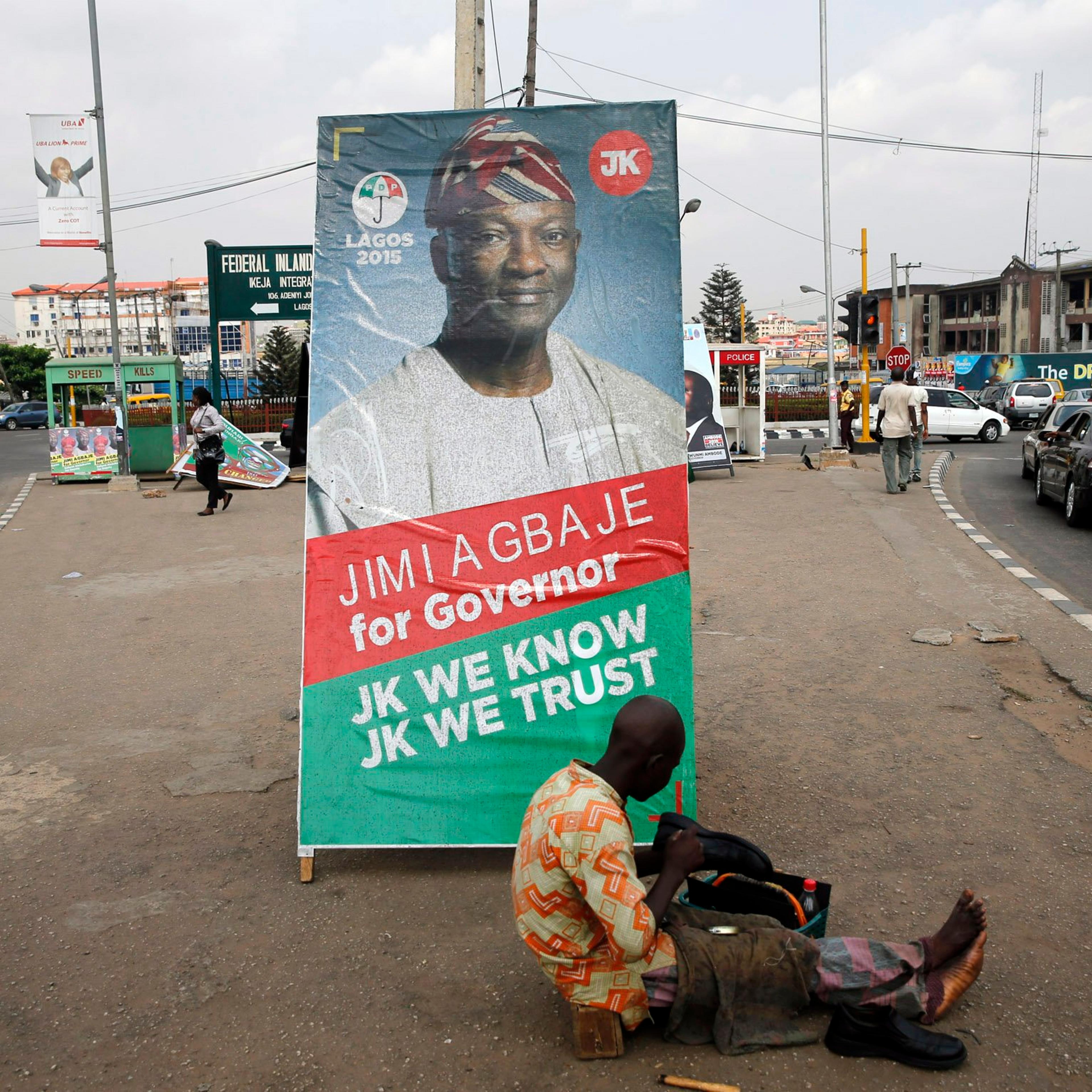 A shoe-mender works near a poster campaigning for Jimi Agbaje, along a road in the Ikeja district in Lagos