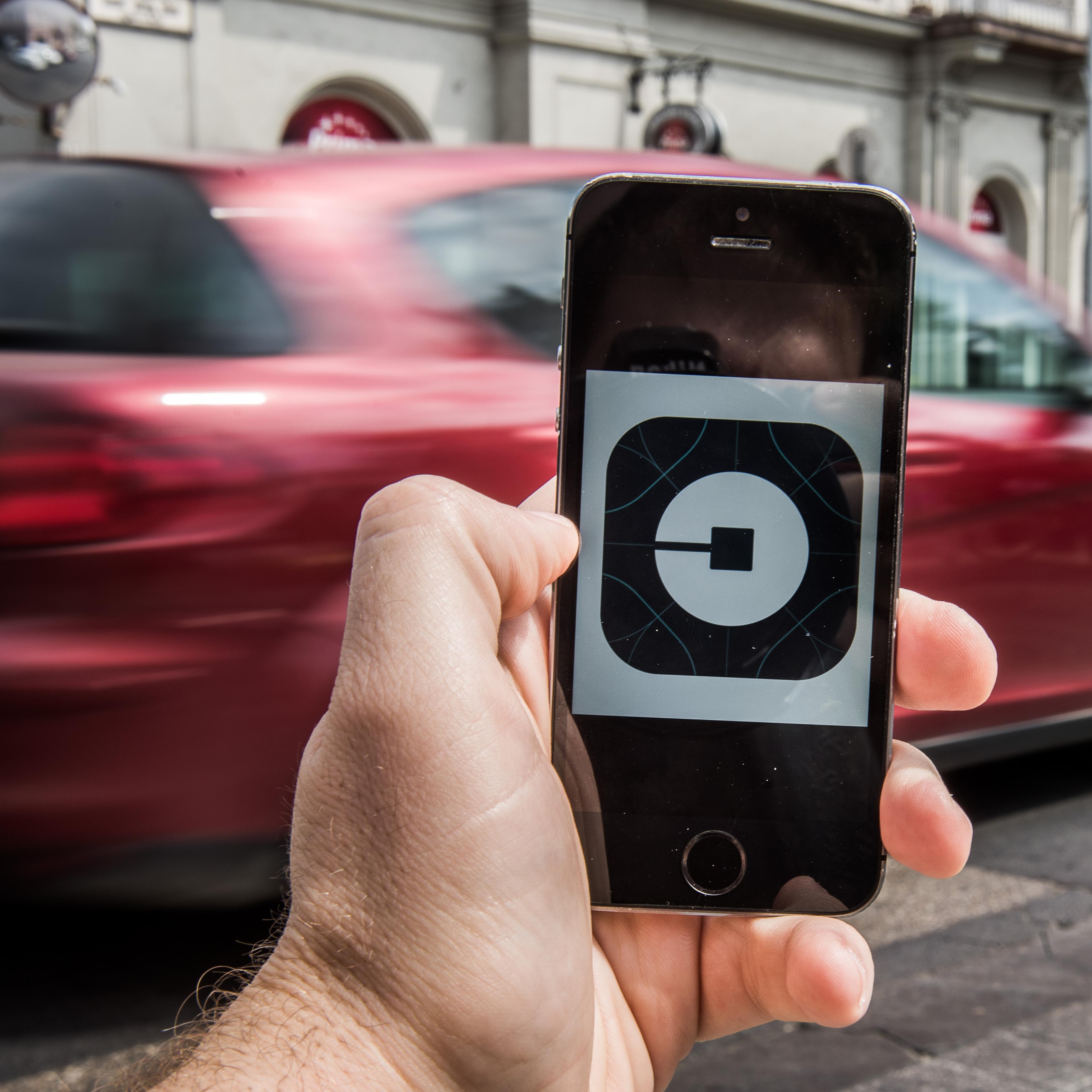 A customer holds an Apple Inc. iPhone displaying the Uber Technologies Inc. car service taxi application (app) logo as a vehicle passes by in this arranged photograph in Budapest, Hungary, on Wednesday, July 13, 2016.