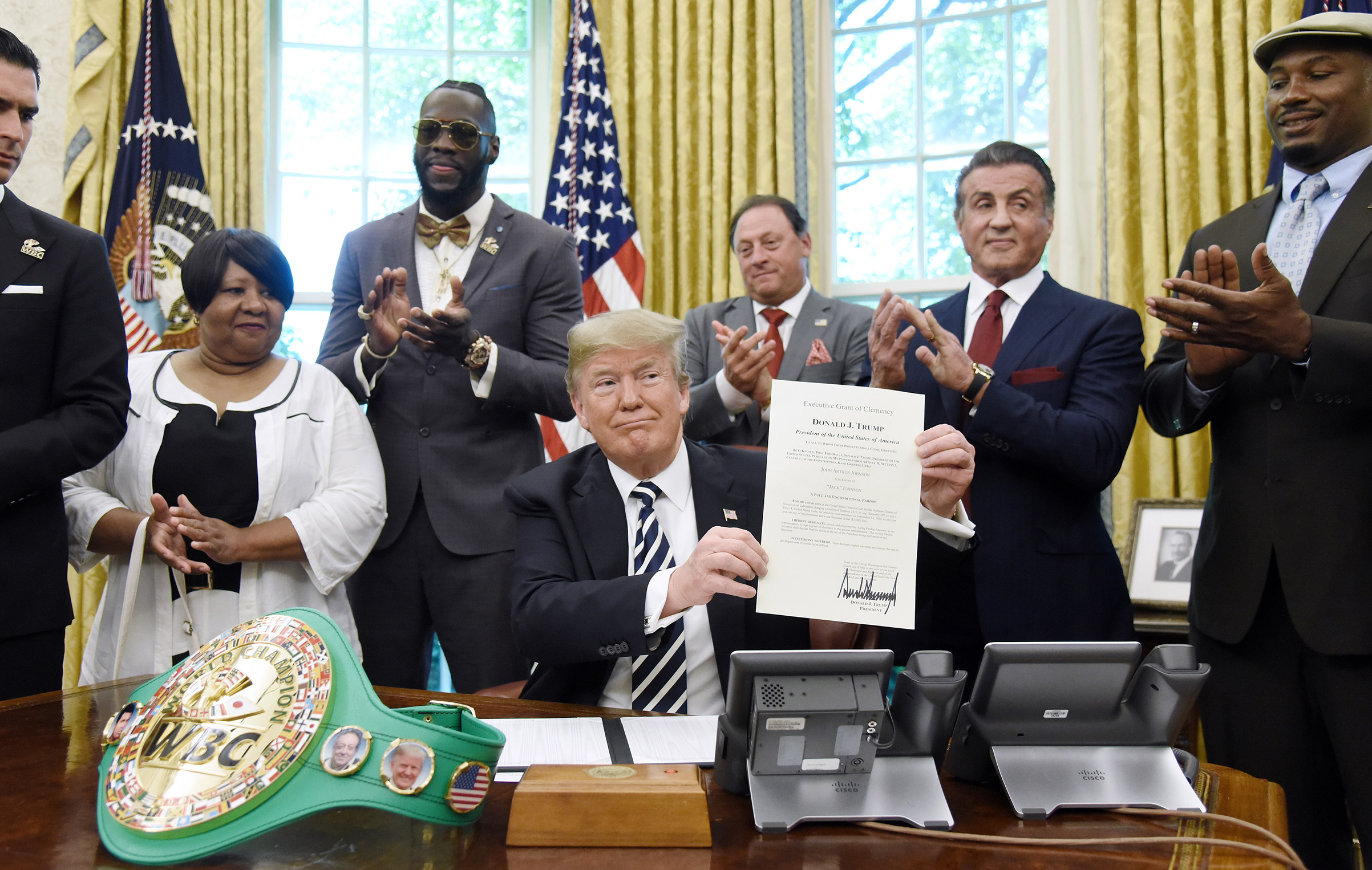 President Donald Trump holds up a signed executive order granting a posthumous pardon for Jack Johnson, the first black heavyweight boxing champion, as boxing champion Lenox Lewis, from left, and actor Sylvester Stallone applaud in the Oval Office of the White House in Washington, D.C., U.S., on May 24, 2018.