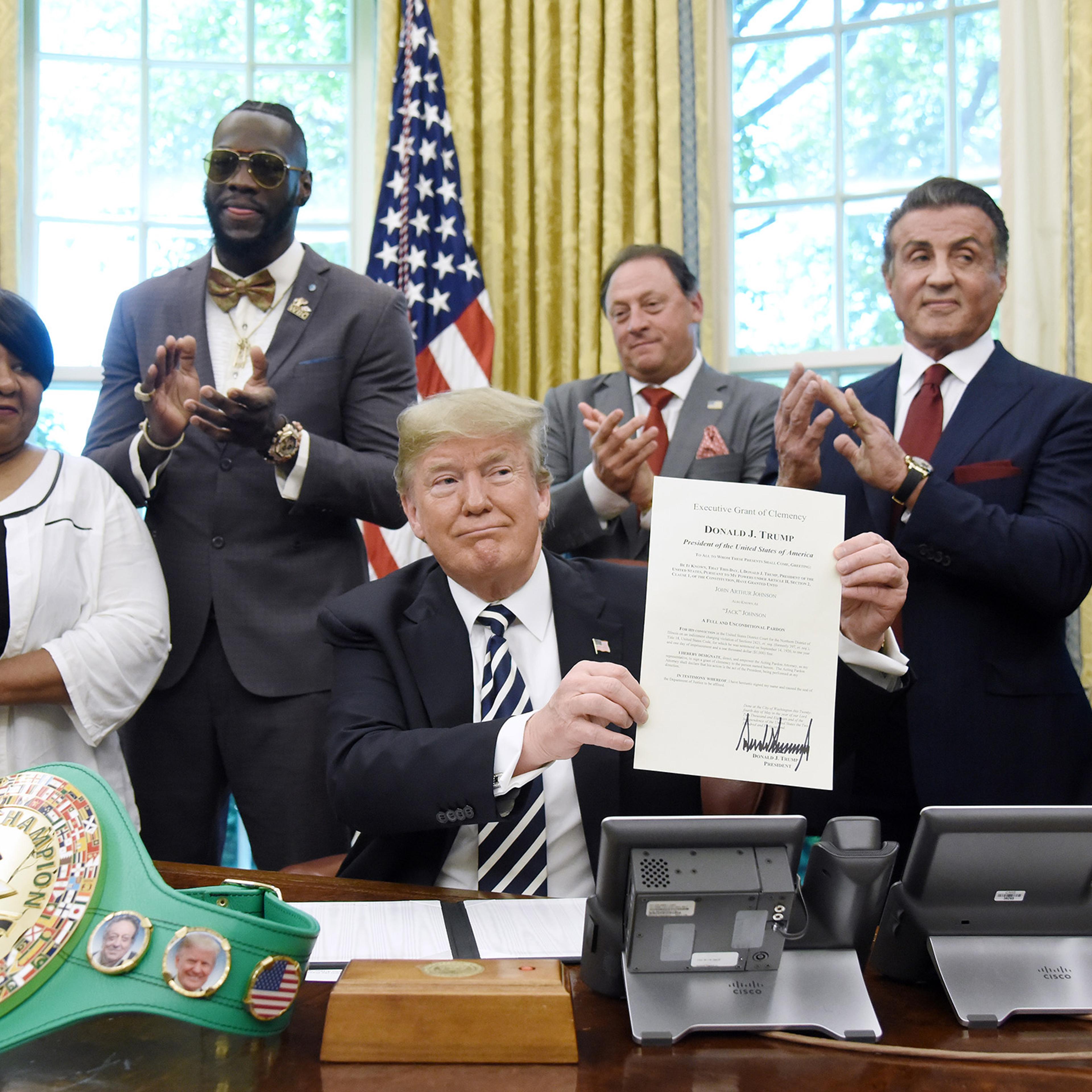 President Donald Trump holds up a signed executive order granting a posthumous pardon for Jack Johnson, the first black heavyweight boxing champion, as boxing champion Lenox Lewis, from left, and actor Sylvester Stallone applaud in the Oval Office of the White House in Washington, D.C., U.S., on May 24, 2018.