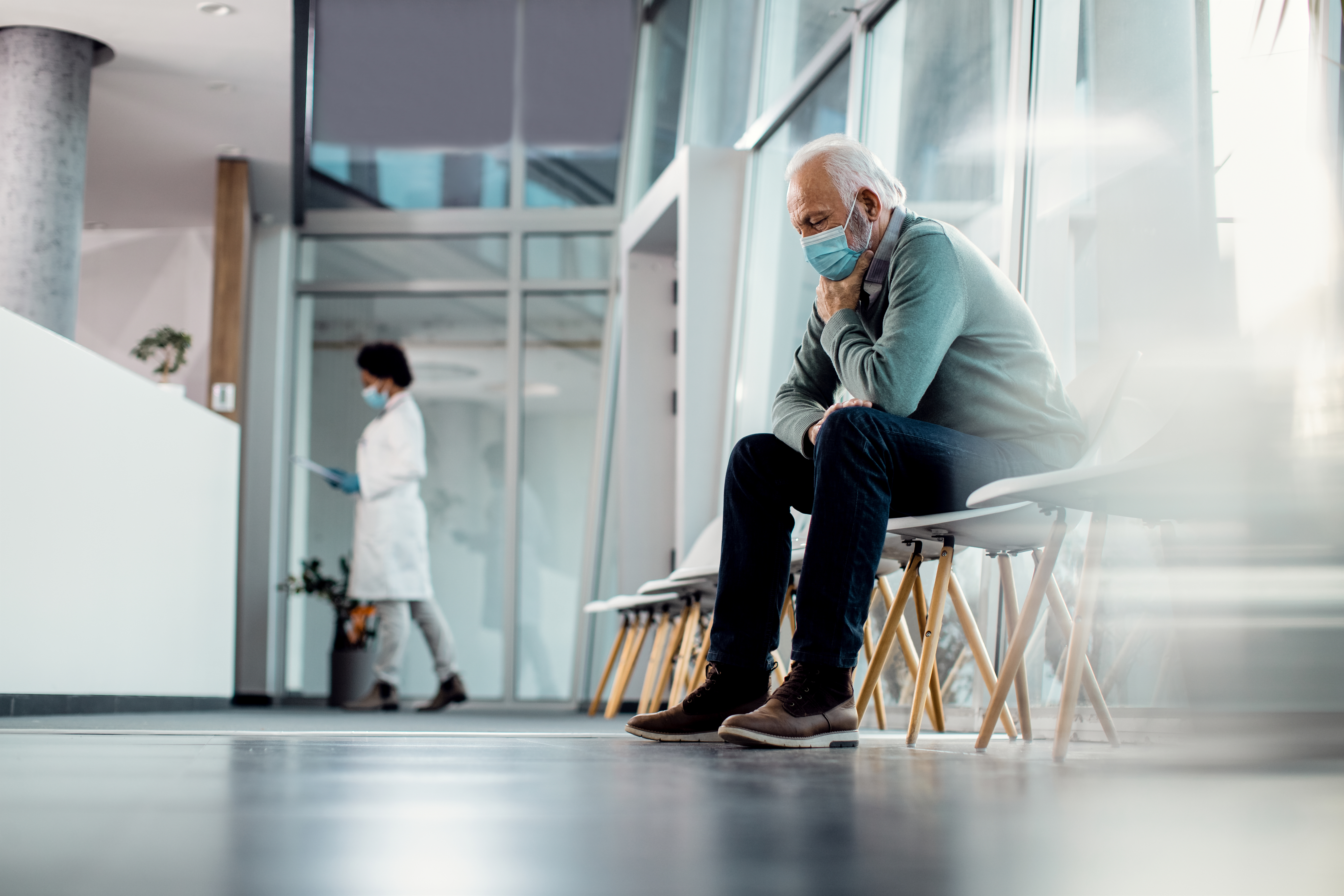 Worried senior man thinking of something while sitting in hospital waiting room during coronavirus pandemic.