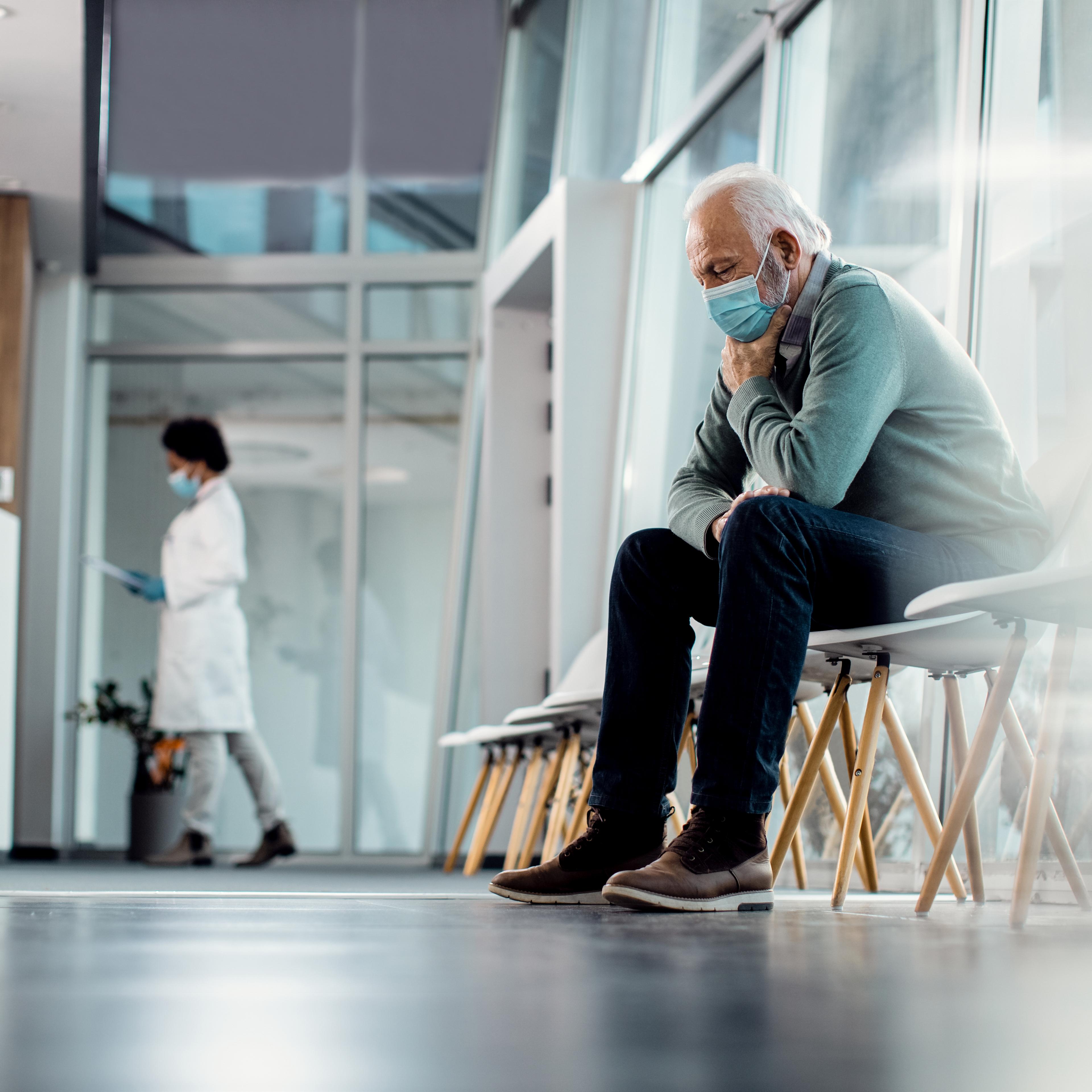 Worried senior man thinking of something while sitting in hospital waiting room during coronavirus pandemic.