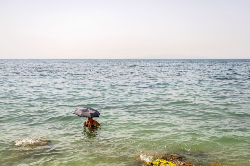 A woman holds an umbrella in the water at Alimos beach near Athens, on July 15, 2023, as Greece is hit by a heat wave, like other several European countries.