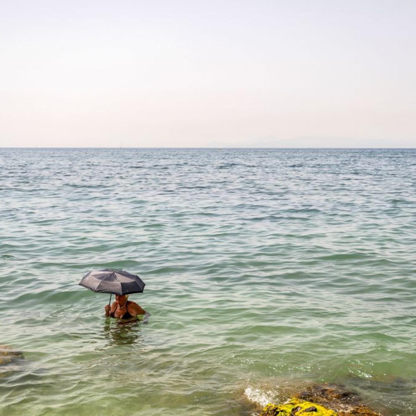 A woman holds an umbrella in the water at Alimos beach near Athens, on July 15, 2023, as Greece is hit by a heat wave, like other several European countries.