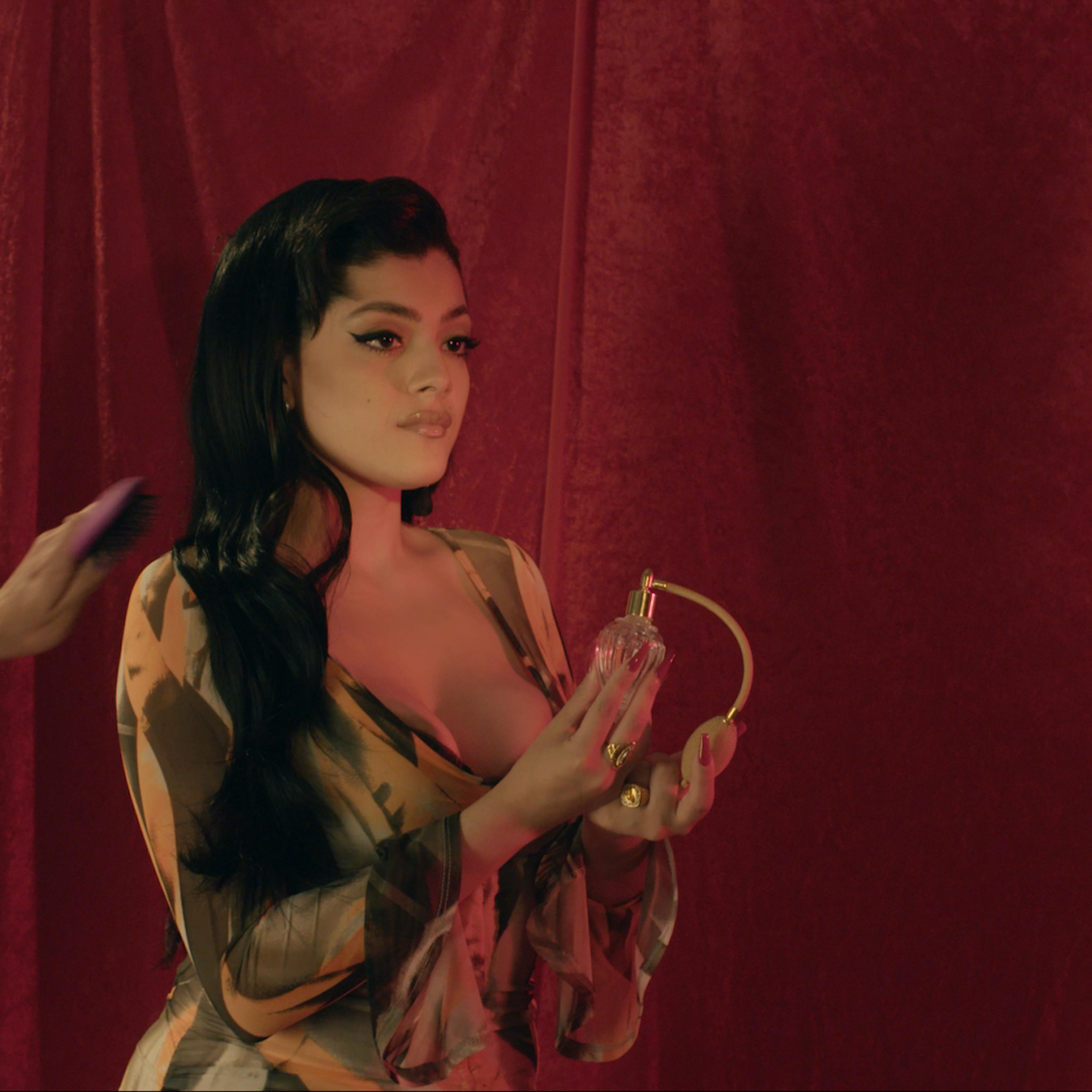 Jacks Haupt poses against a red velvet backdrop in a low-cut yellow dress with flowing sleeves.