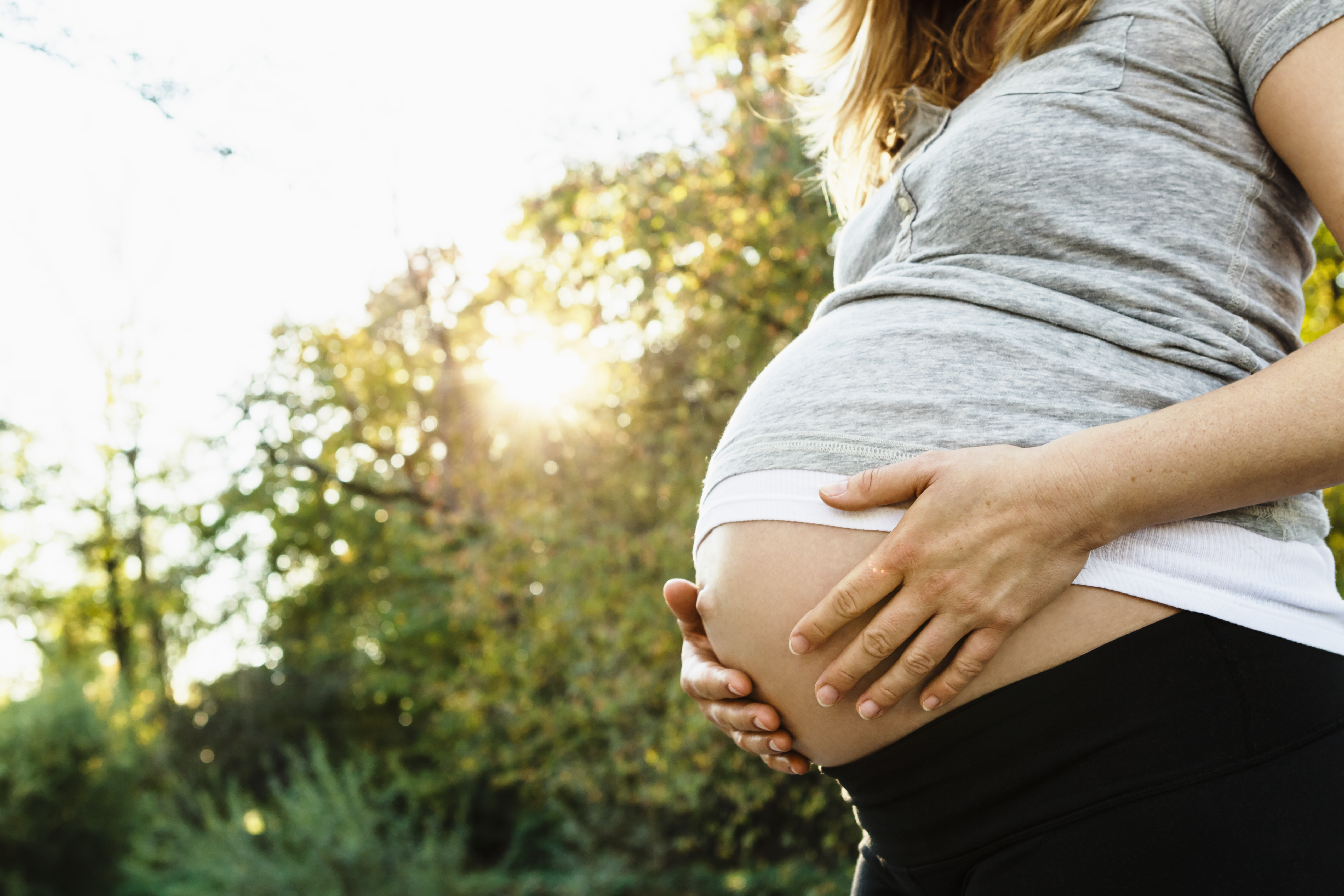 Pregnant woman holding belly, outdoors, mid section