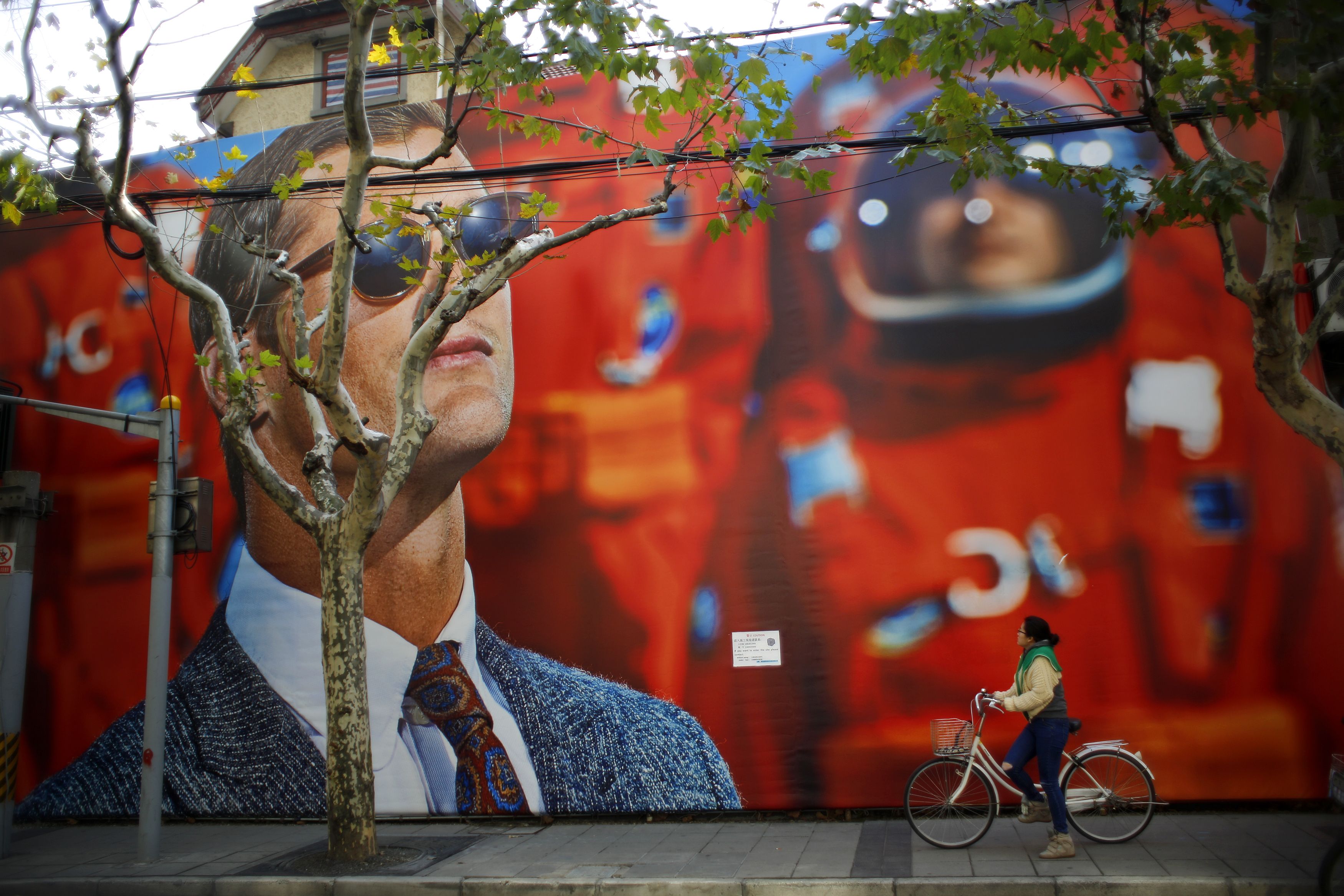 A woman looks at a giant billboard for a clothing shop, as she rides her bike along a street in downtown Shanghai