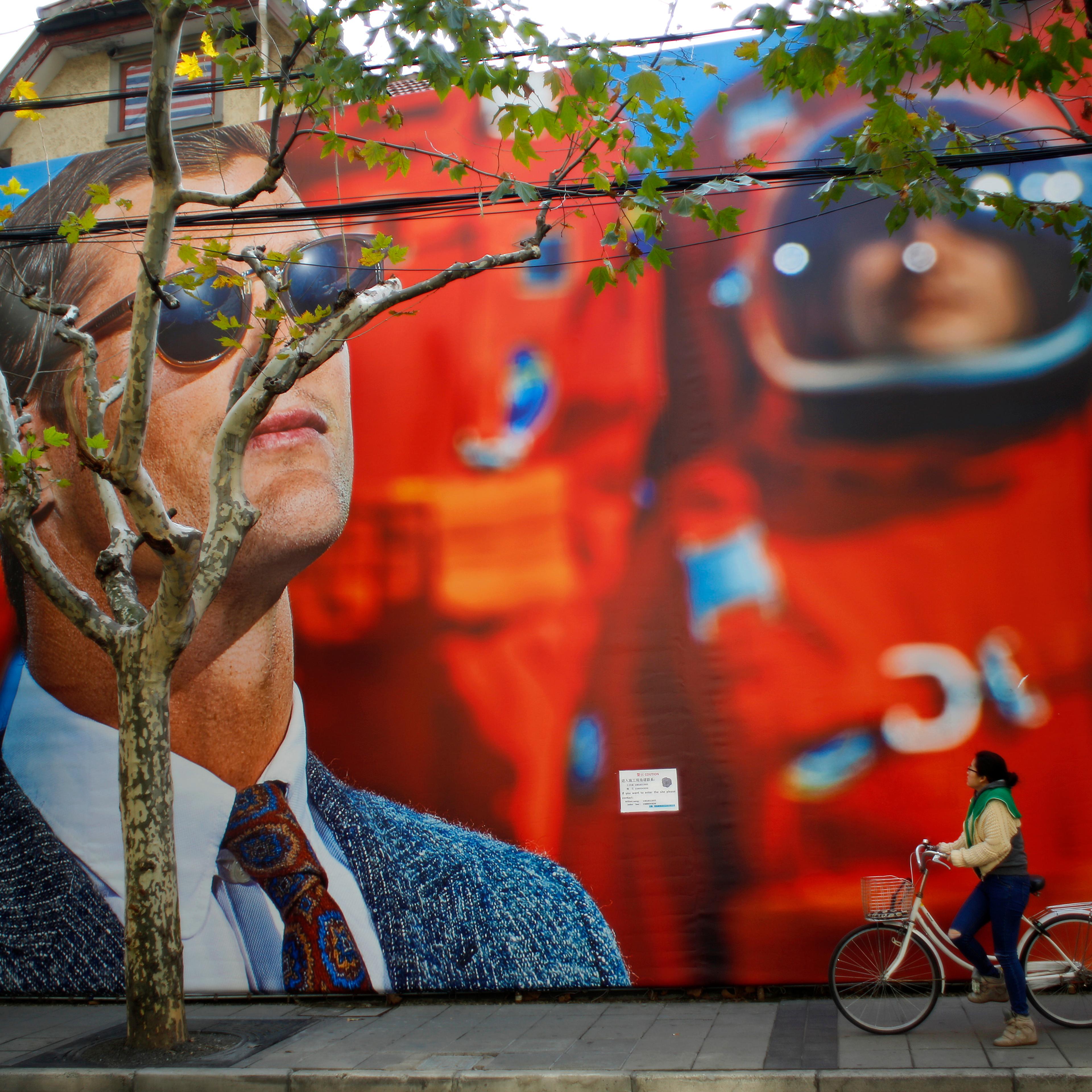 A woman looks at a giant billboard for a clothing shop, as she rides her bike along a street in downtown Shanghai