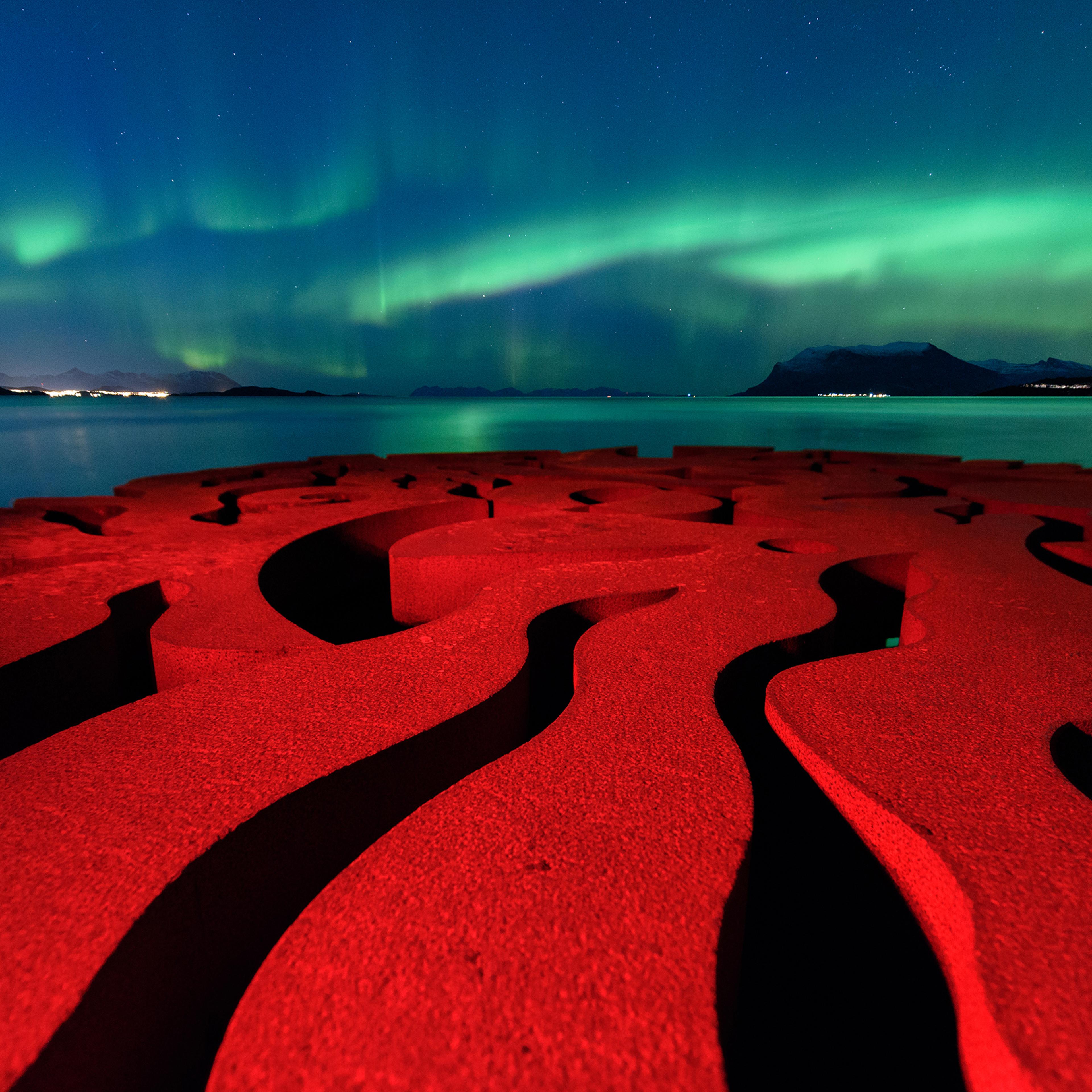 The rusty red swirls of the circular, iron sculpture, Seven Magic Points, in Brattebergan, Norway, mirror the rippling aurora above.