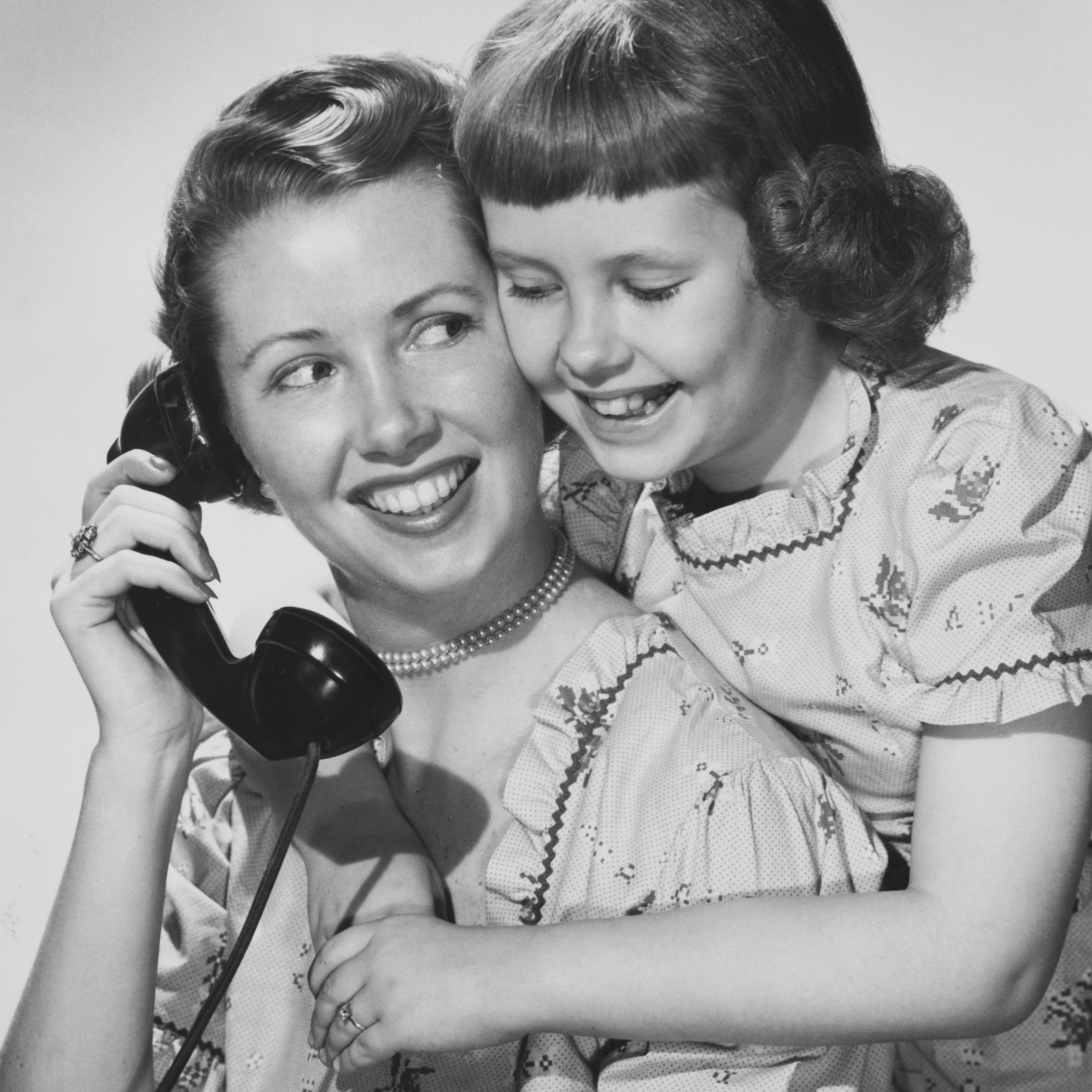 Mother holding telephone and hugging daughter (12-13)